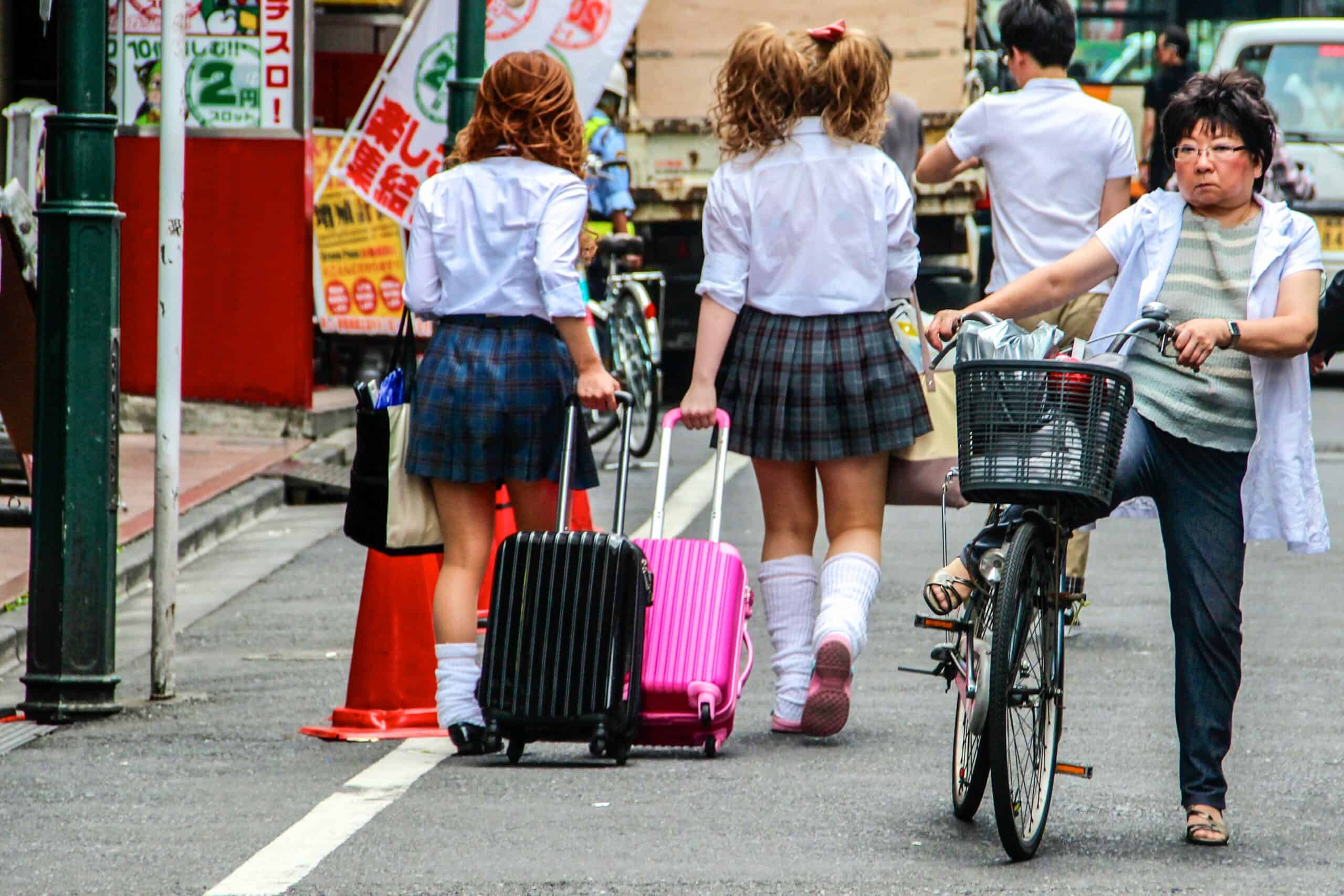 Two girls with matching school outfits and black and pink suitcases in Harajuku, Tokyo, Japan. 