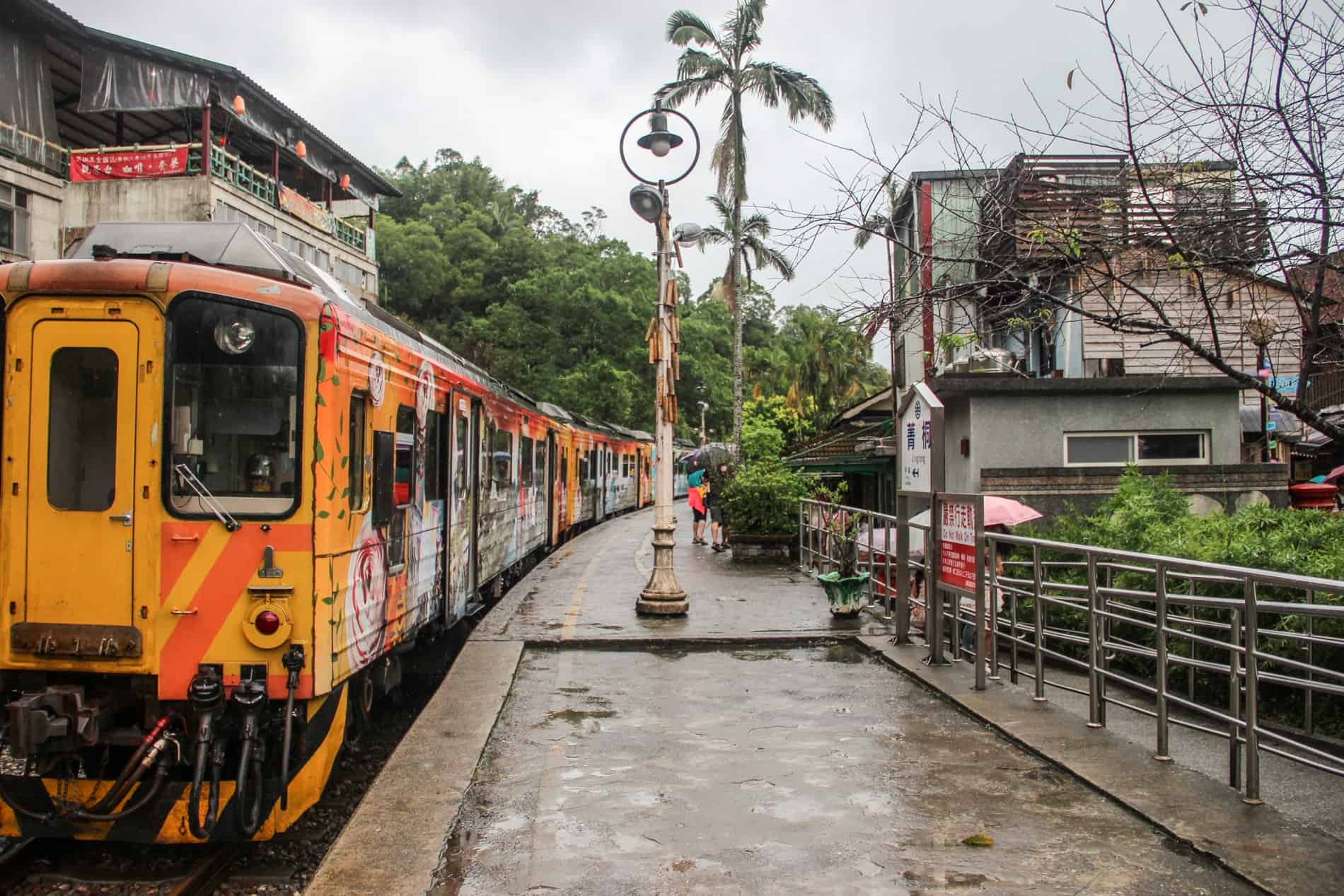 A orange train waiting at a timeworn platform at the heritage Jingtong Train Station.