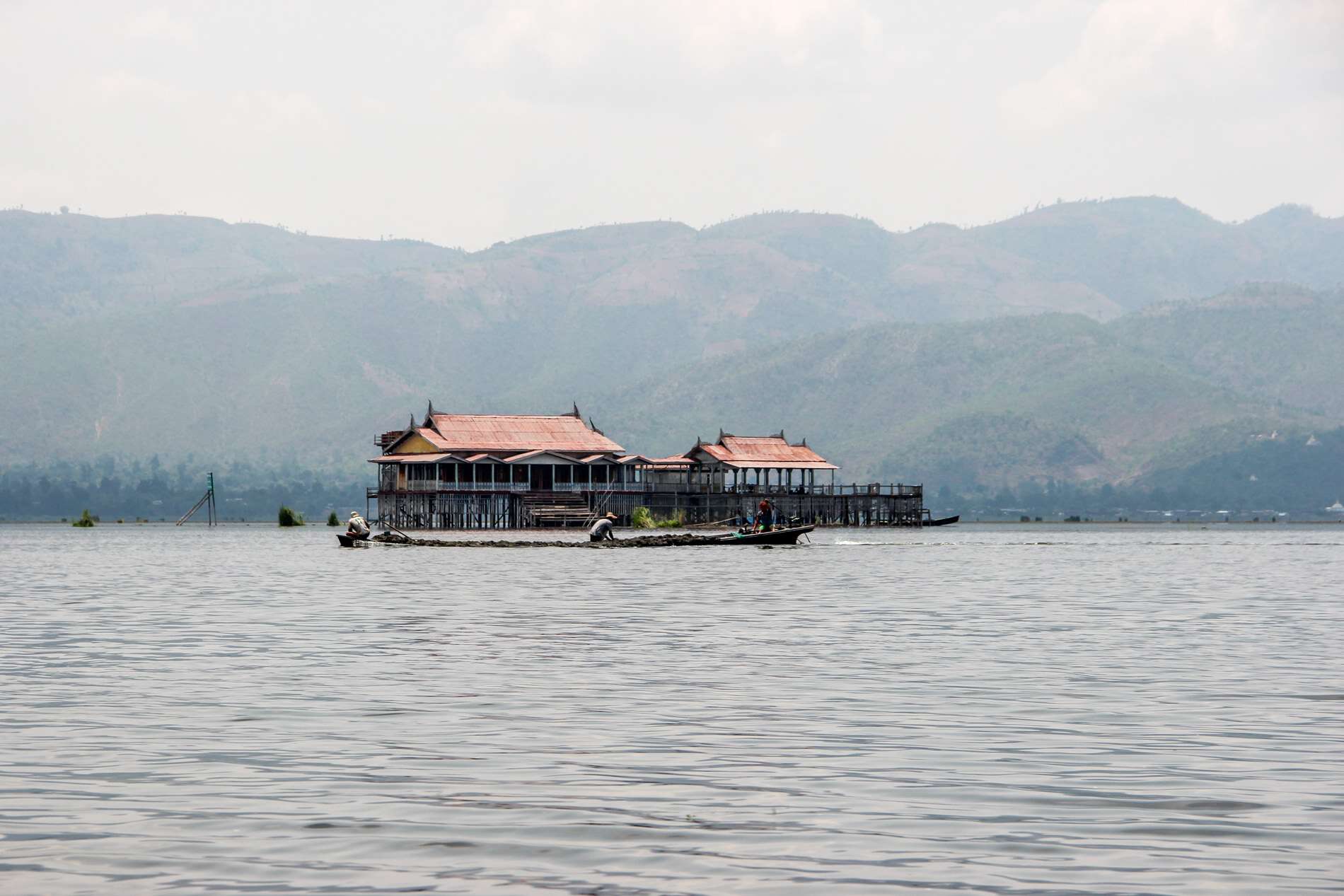 In front of a large stilt house in the middle of the vast Inle Lake, men build a mound of soil on the water, for the creation of a floating garden. 