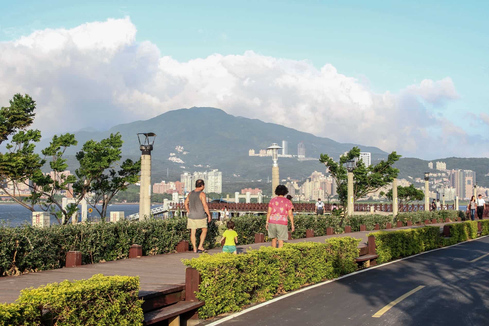 People strolling in a promenade park to a mountainous backdrop in Bali, New Taipei. 