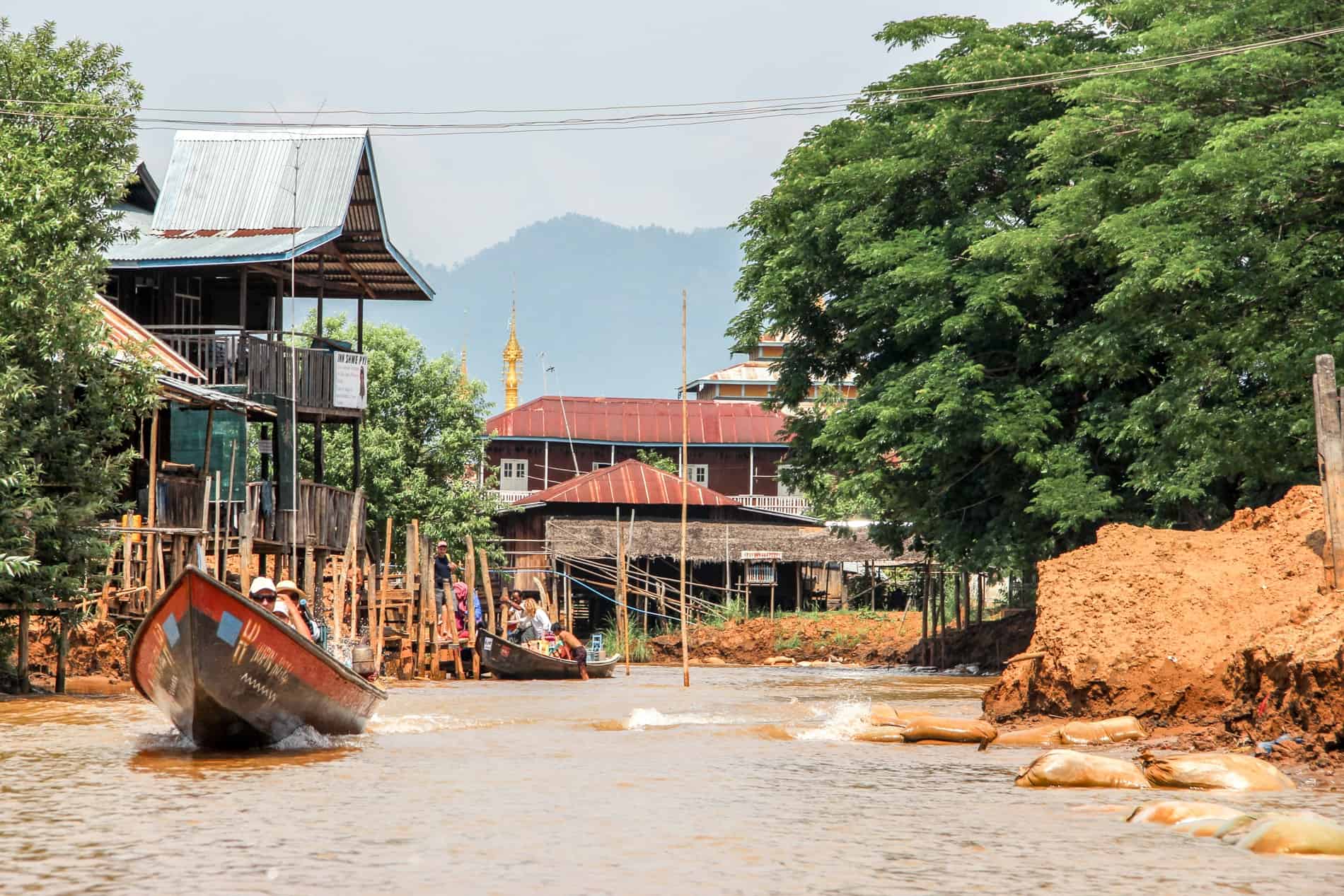 Boats of tourists on a shallow water canal on Inle Lake with bamboo stilt houses lining the banks. 