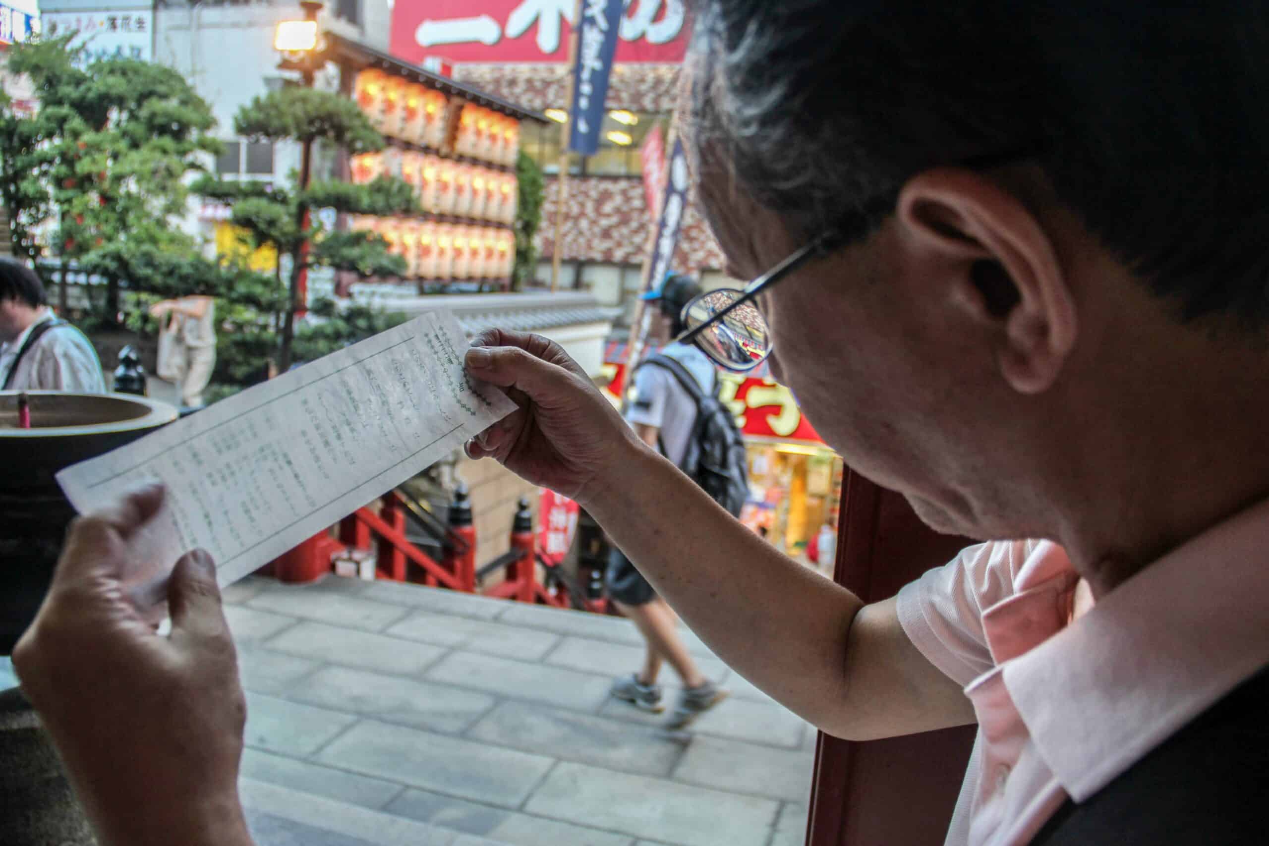 A Japanese man reads his fortune from a white prayer paper at a temple in Tokyo, Japan.