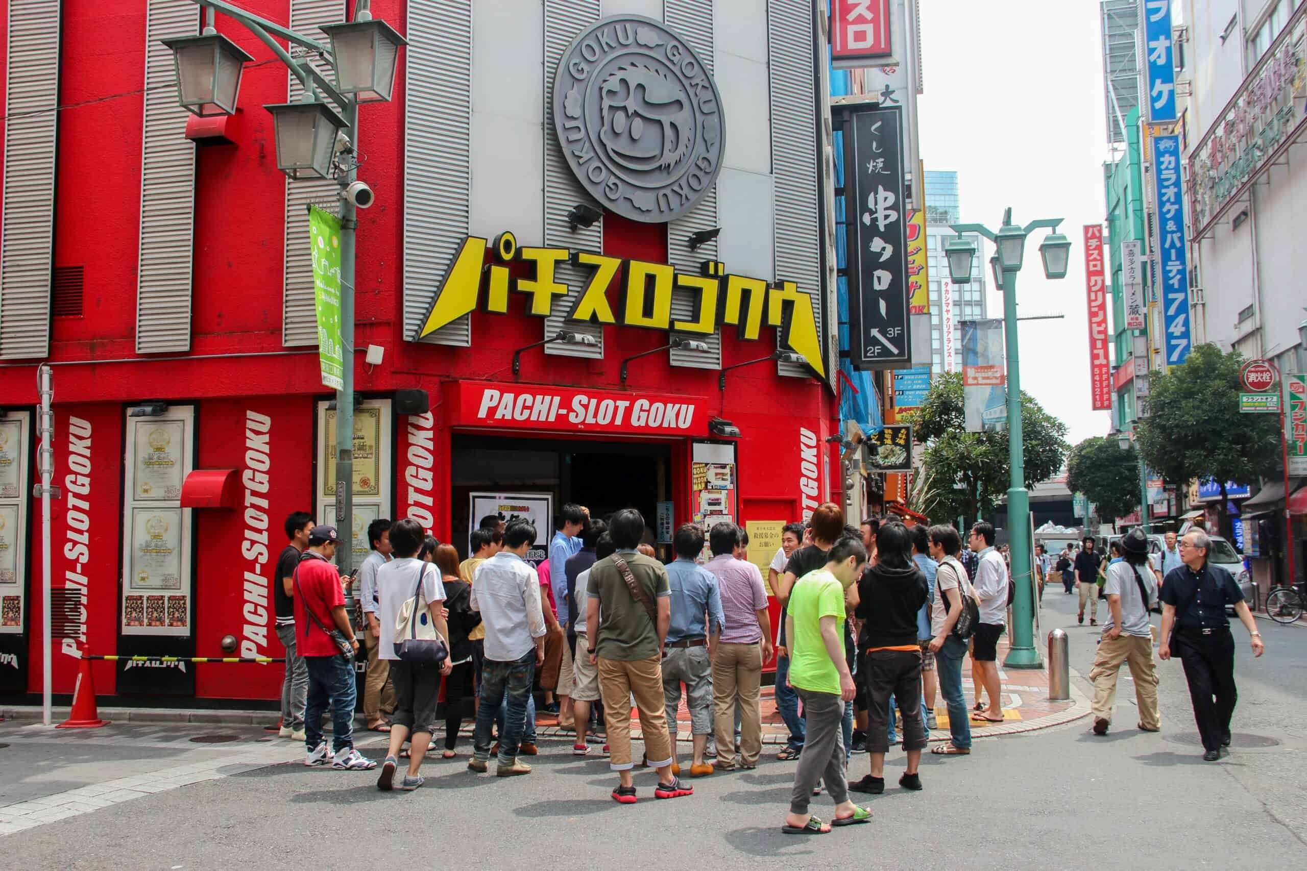 A group of people gather outside a red Pachinko slot machine arcade in Tokyo.