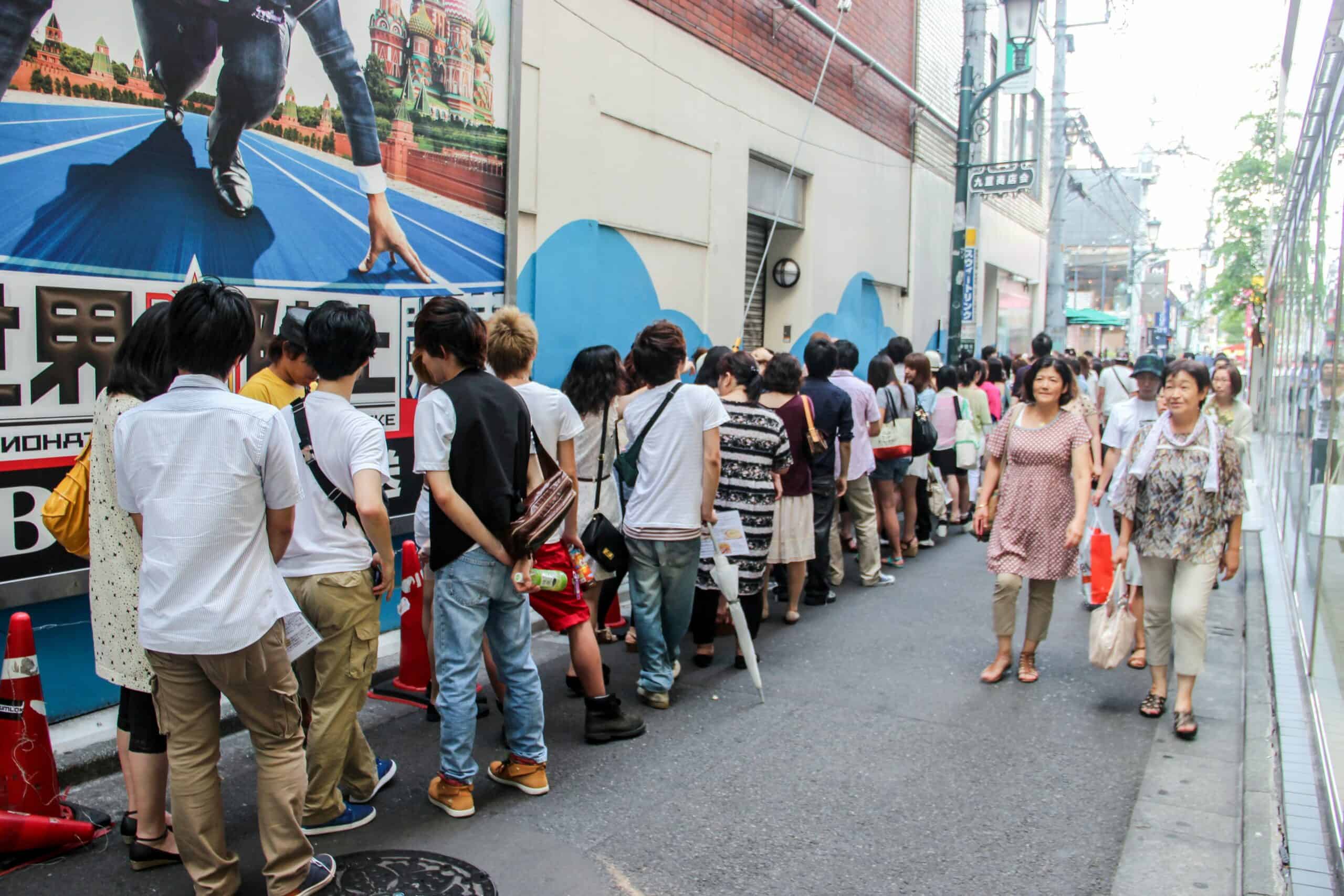 Two Japanese women walk past a long and orderly line of young people outside a building in Tokyo.