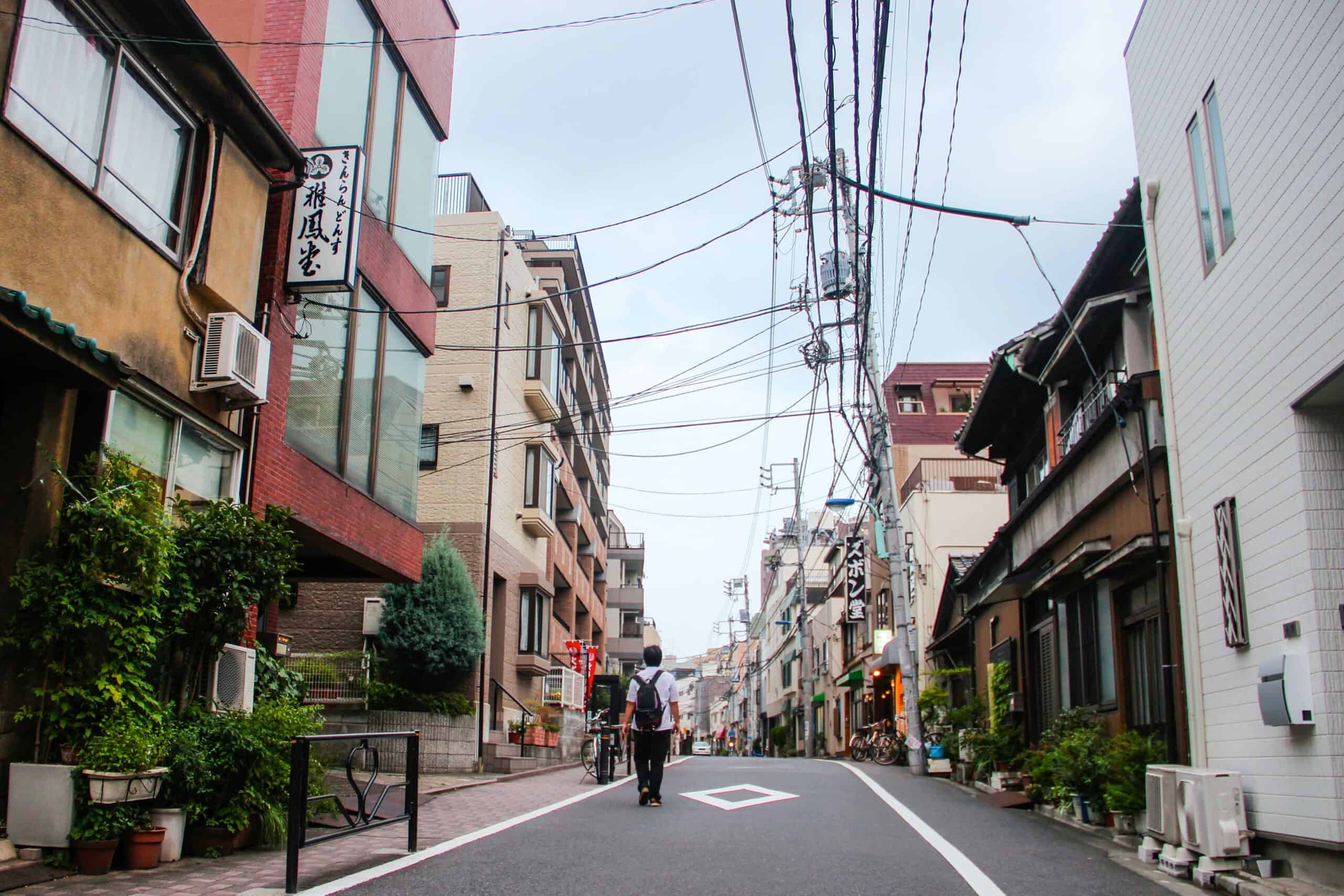 A man walks down a residential street of Tokyo, Japan with neat, compact box design buildings.