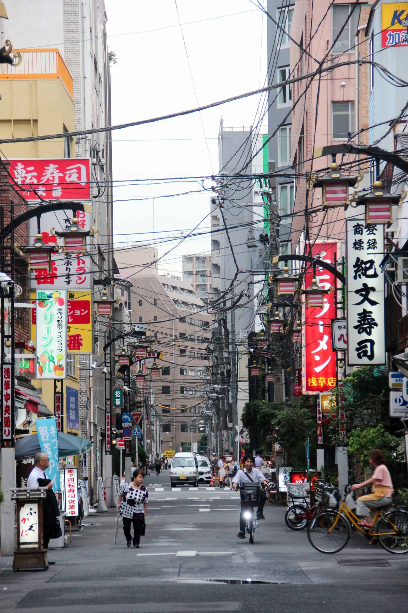 A street road in Tokyo lined with large neon signage and black wires. 