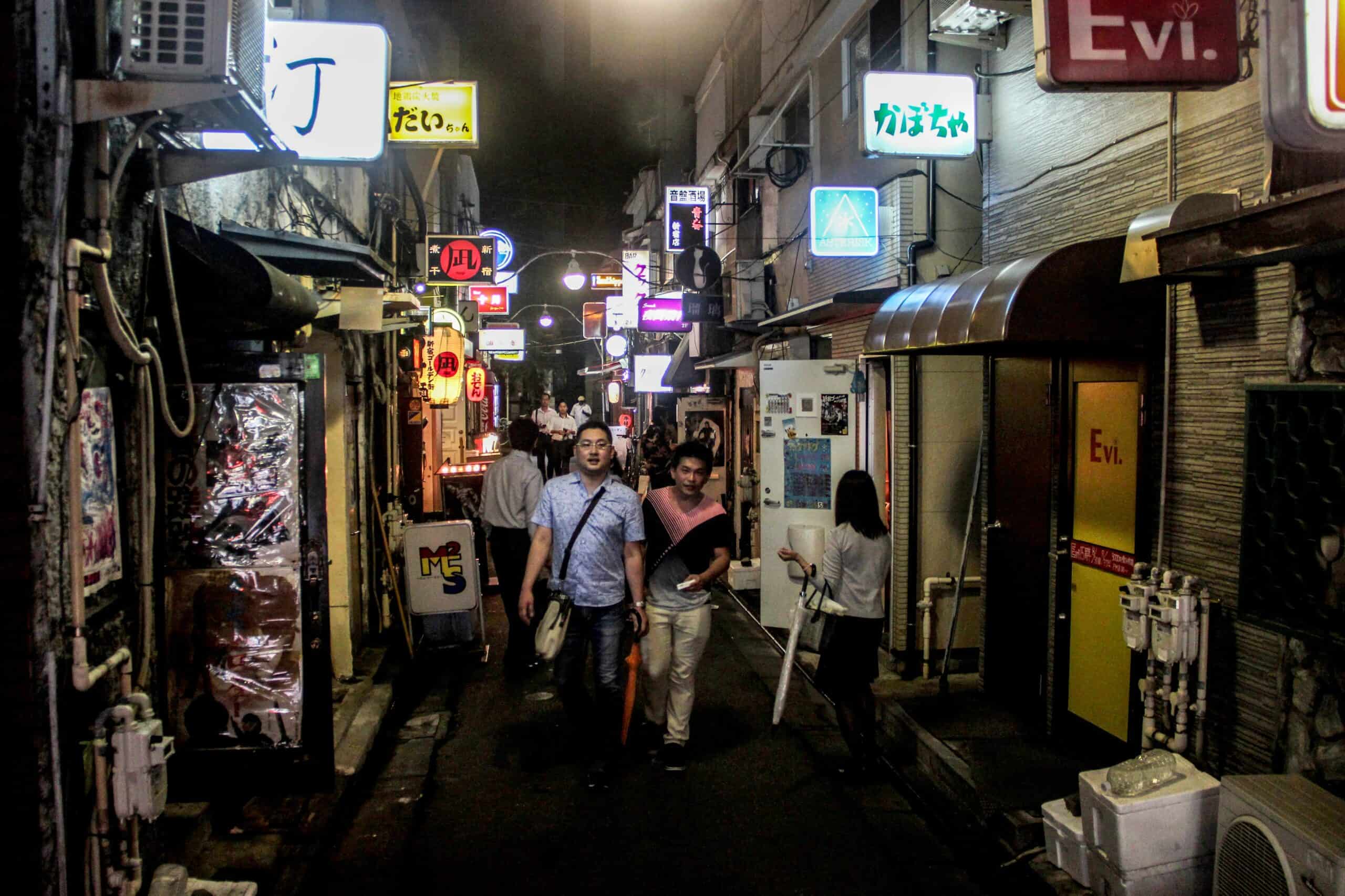 People walking down the narrow alleyways of bars with lit neon signs in Golden Gai, Tokyo.