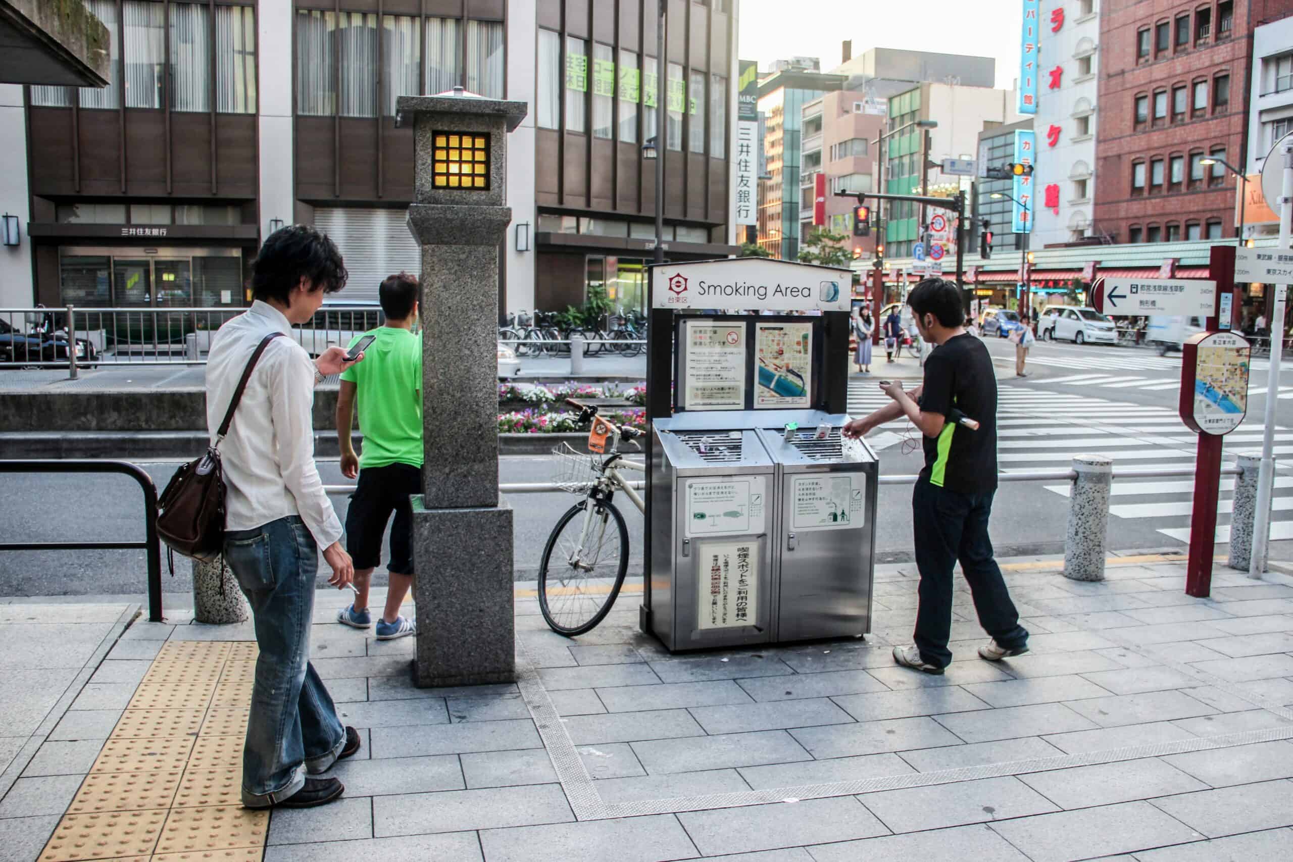 A man puts his cigarette waste into a 'Smoking Area' bin on a street in Tokyo. 