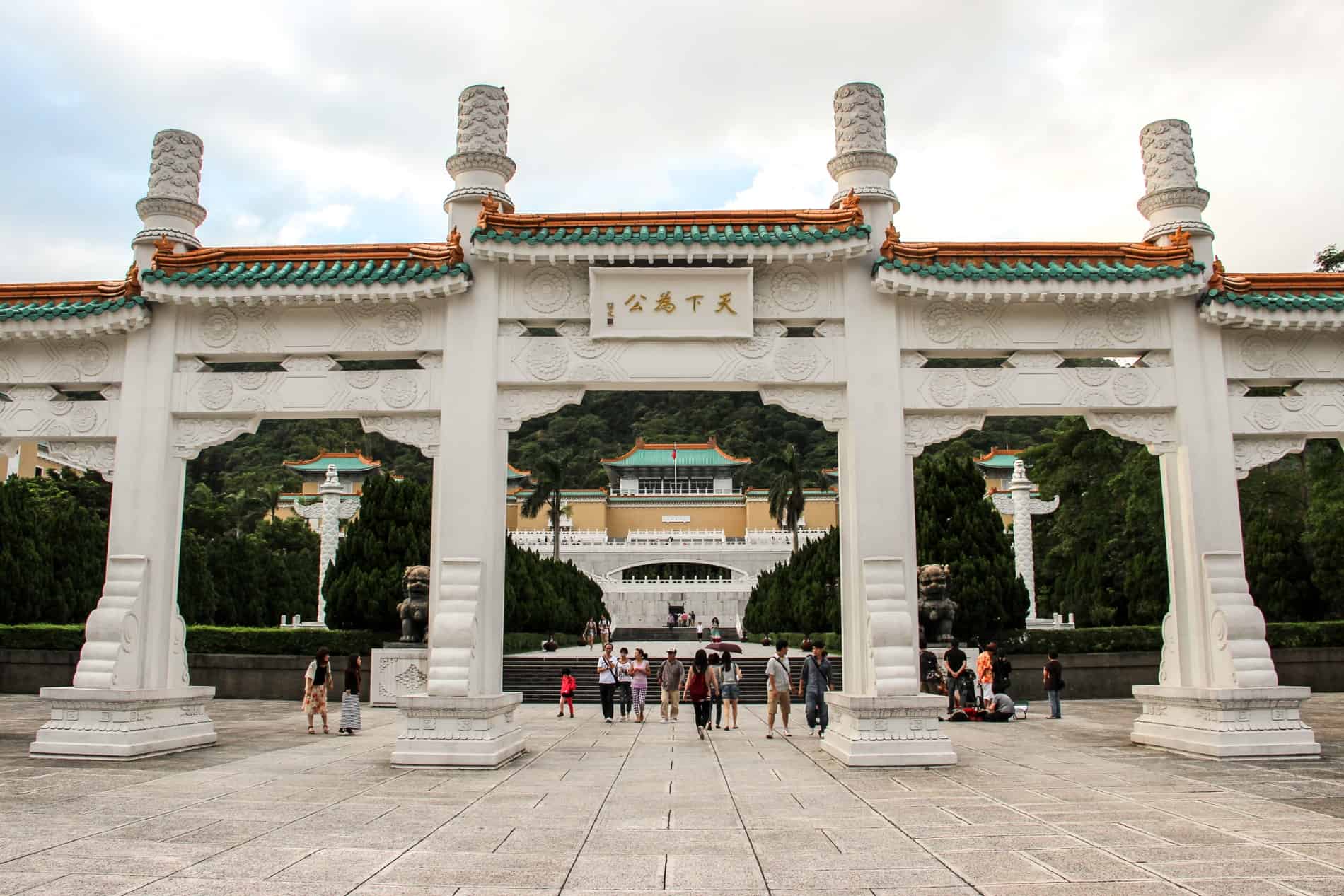 A white stone archway in front of the gold Taiwan National Palace Museum building set within trees. 