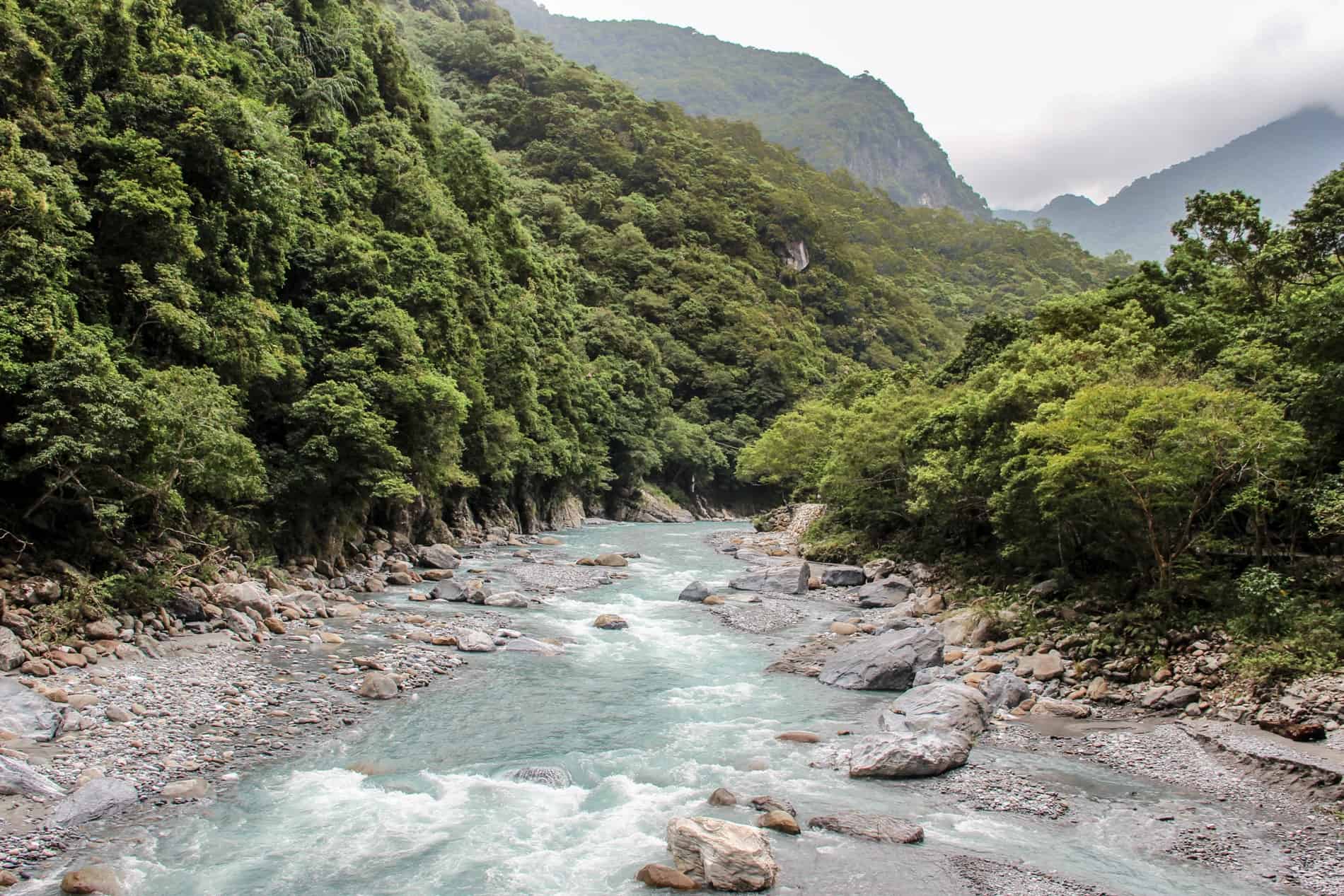 A low rise, rocky river cutting through a gorge of forested slopes. 