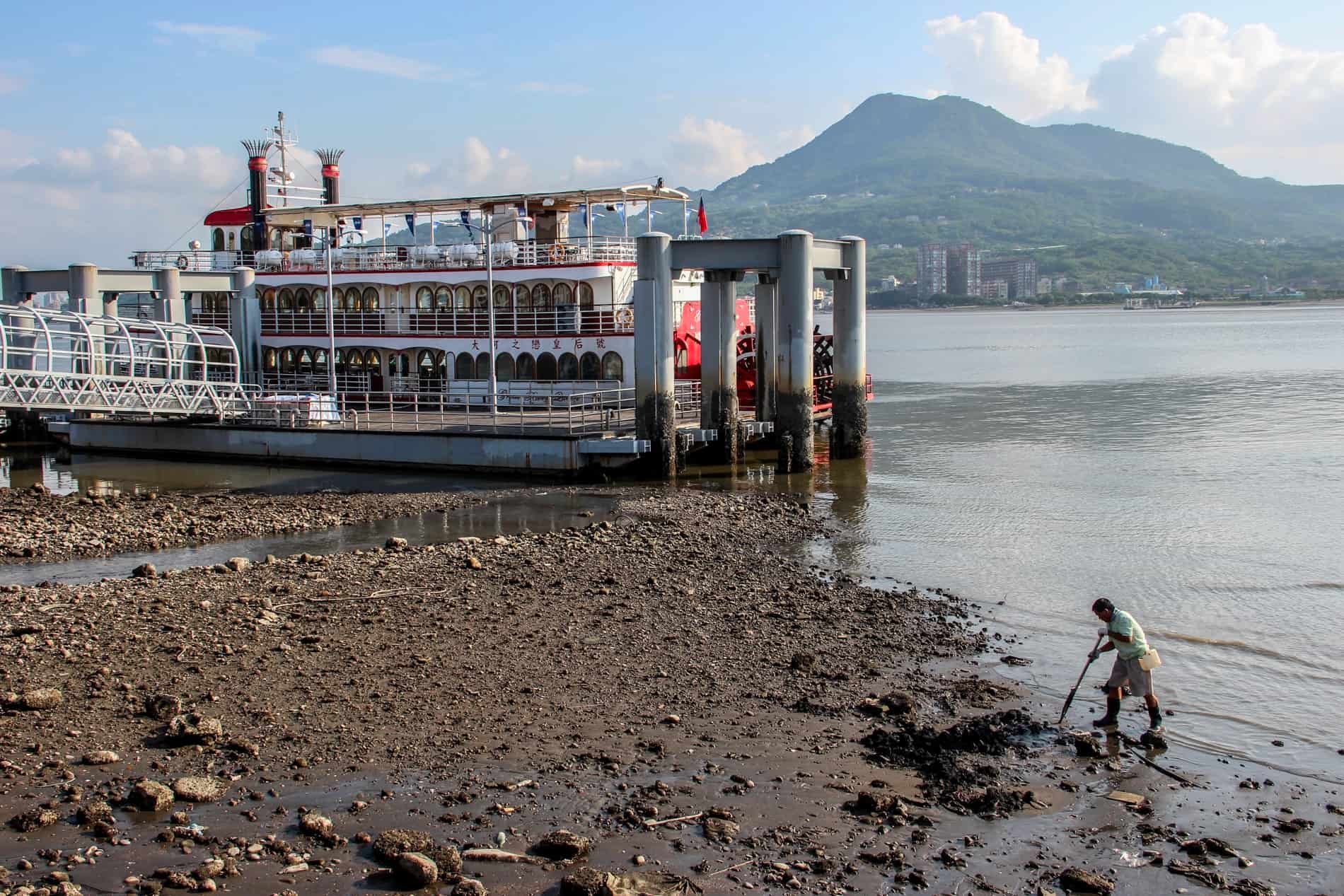 A large triple decker passenger ferry at a dock in Taipei, to a backdrop of mountains. 