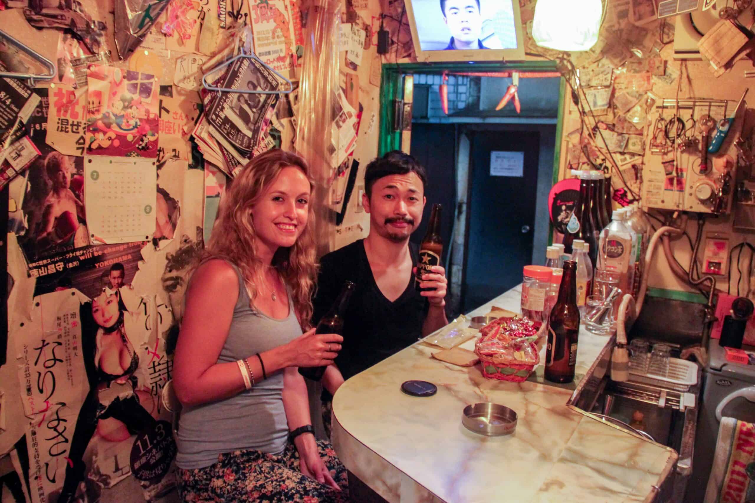 A Japanese man and western woman drinking a bottle of beer in a tiny bar in Shinjuku Golden Gai, Tokyo. 