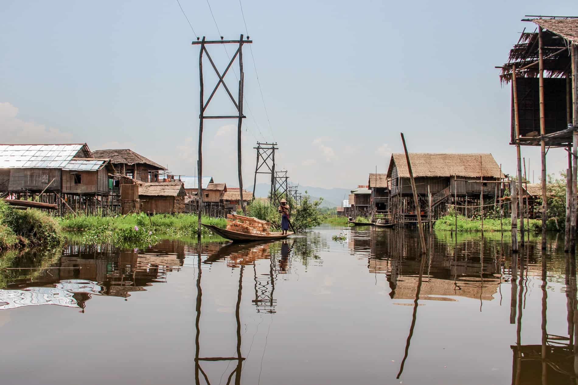 A man rows a long wooden boats through waters lined with bamboo stilt houses belonging to the Intha people of Inle Lake. 