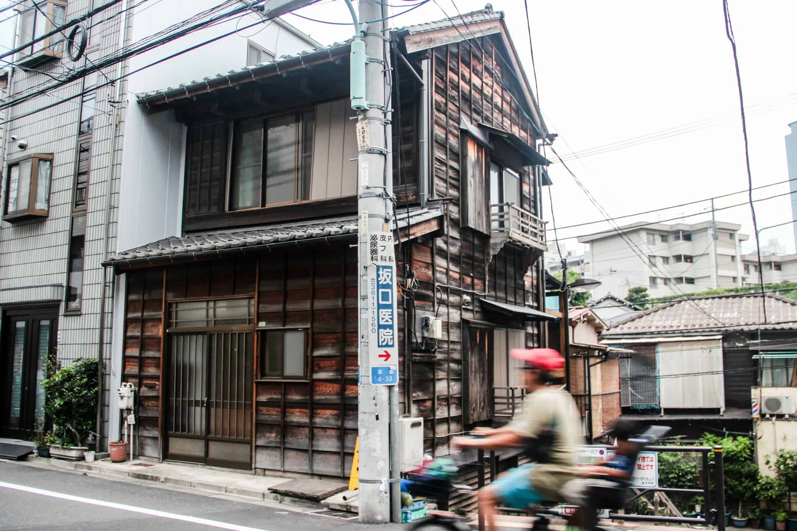 A man of a bike cycles past an old, wooden house found in Tokyo, Japan.