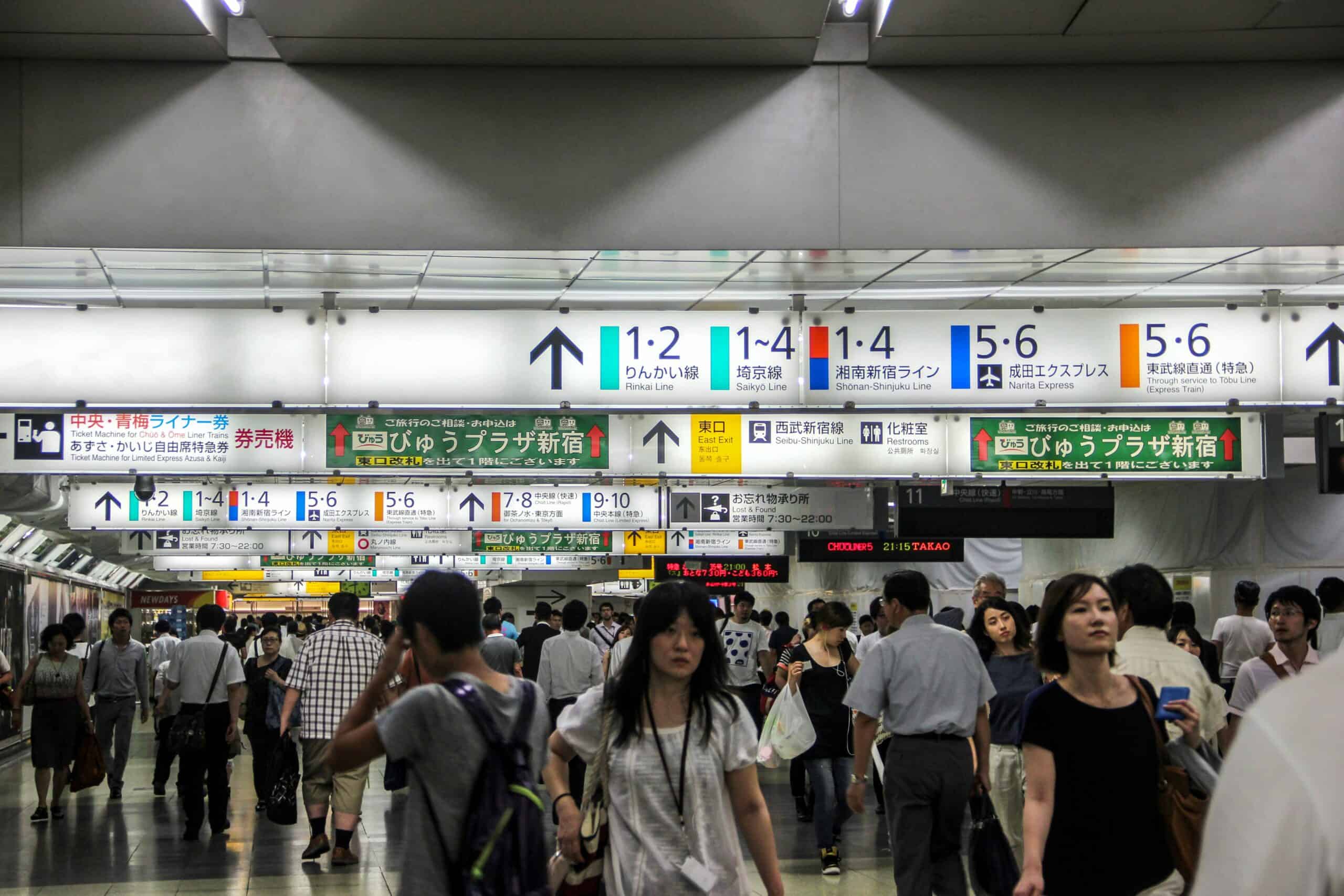 A mass of people walking through the Tokyo metro system in Japan under endless rows of signs with platforms numbers and arrows.