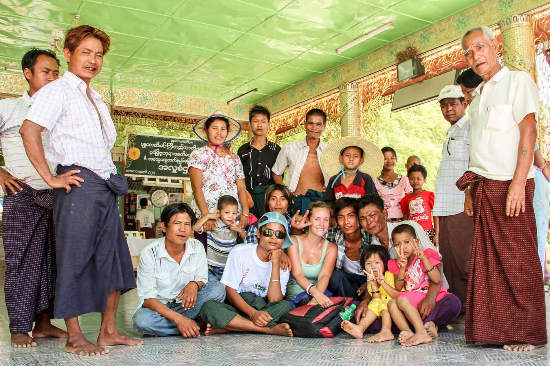 A woman in a mint green top sits on the floor on a green temple room surrounded by a group of Burmese people. Two men stand on the left, and two men and one woman are standing on the right. 