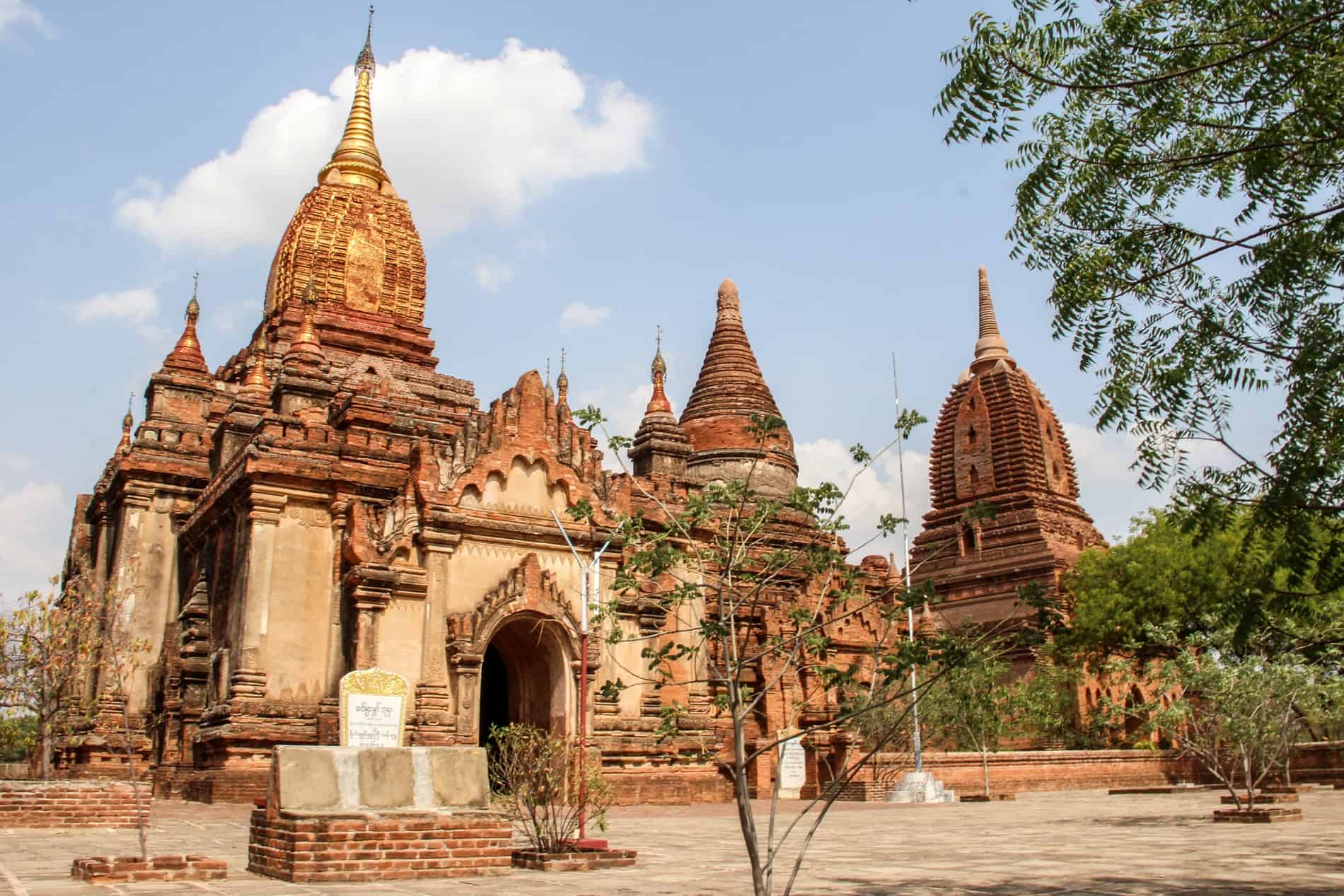 An ochre red brick temple complex in Bagan with three prominent pagoda spires. 