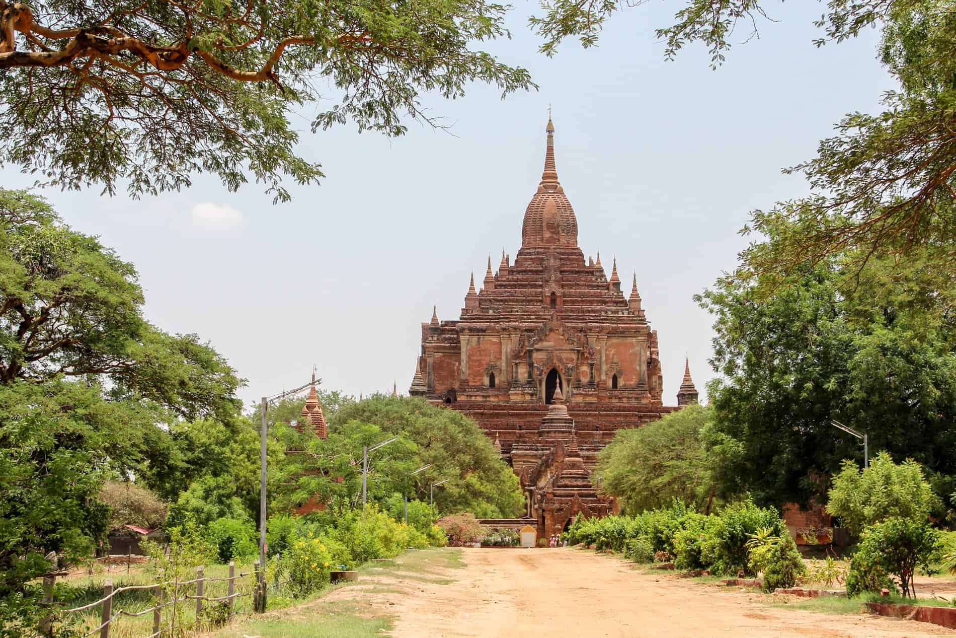 A tree-lined dusty pathway leading to the tiered brick Sulamani Temple in Bagan. 