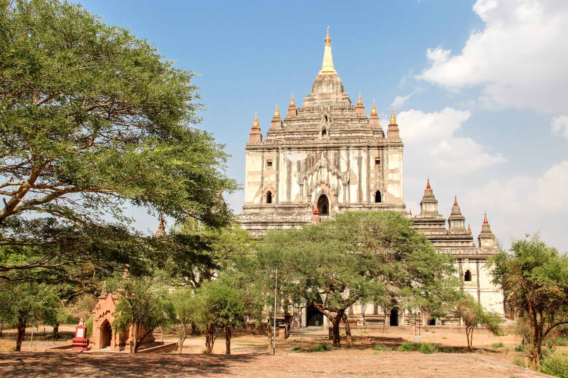 The large tiered and spired white That Bin Nyu Temple in Bagan, set amongst trees. 