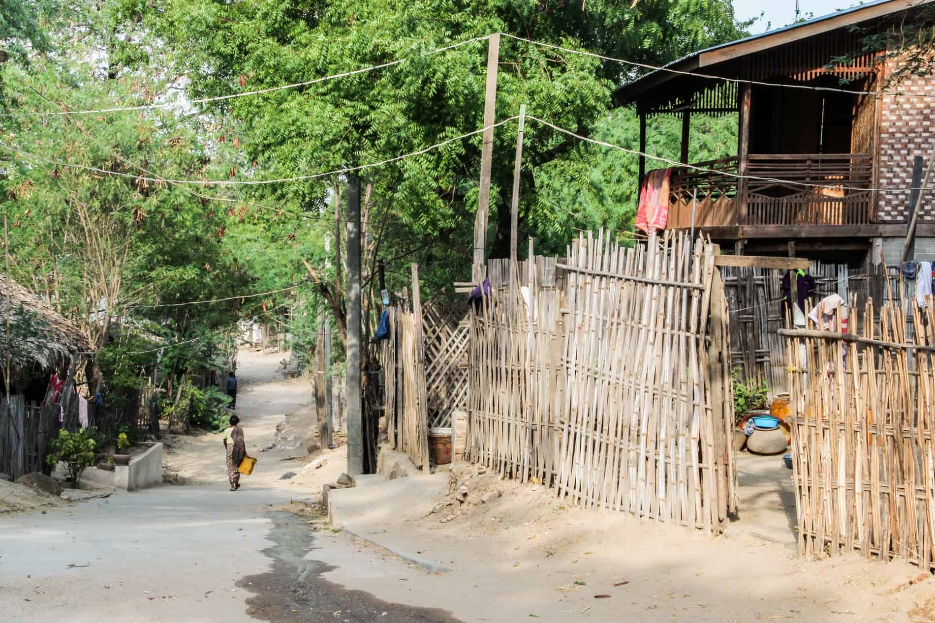 A woman walks down a pathway next to a thatched, wooden house in rural Old Bagan. 