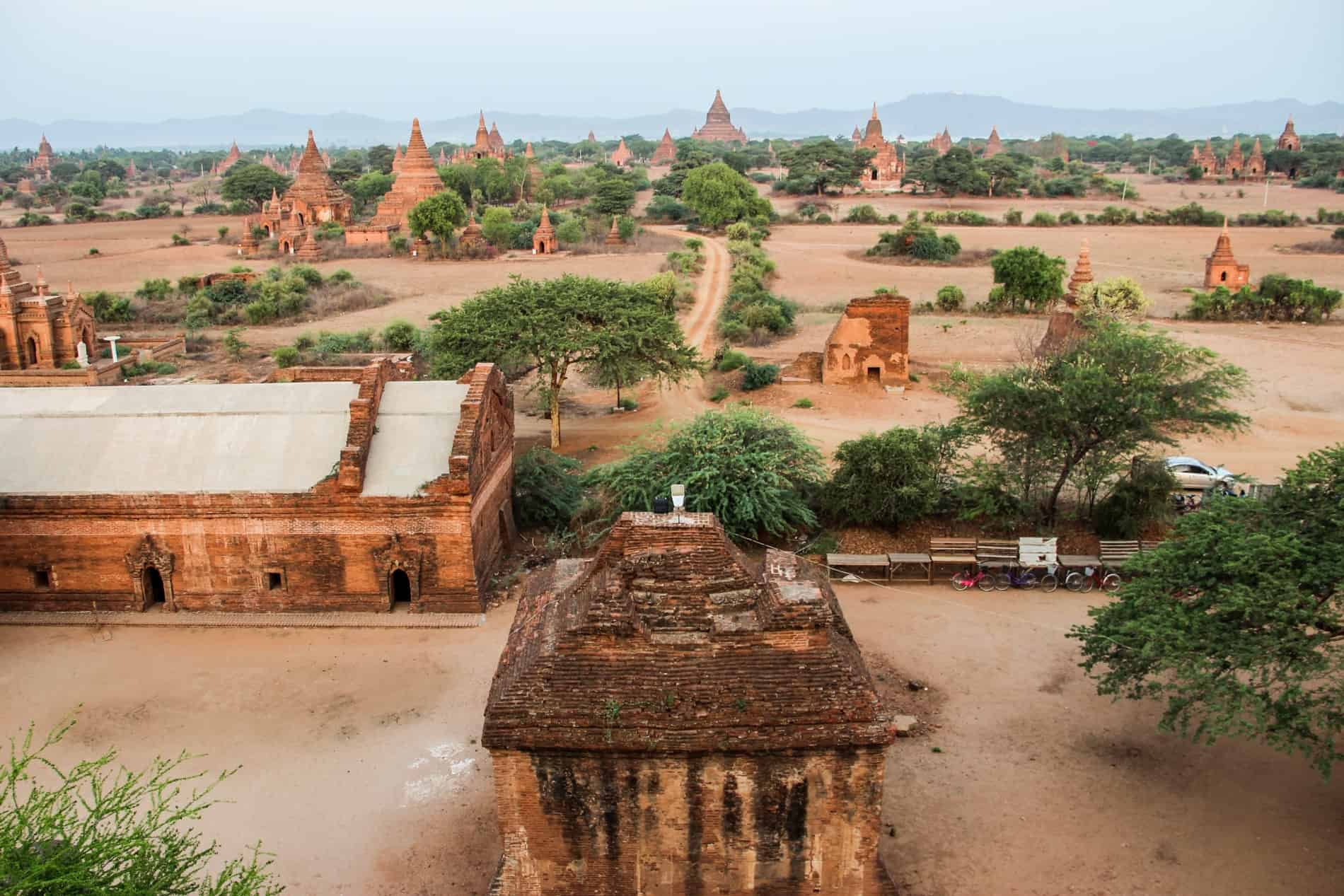 A ochre plain scattered with trees and dozens of orange brick temples with pointed stupas.