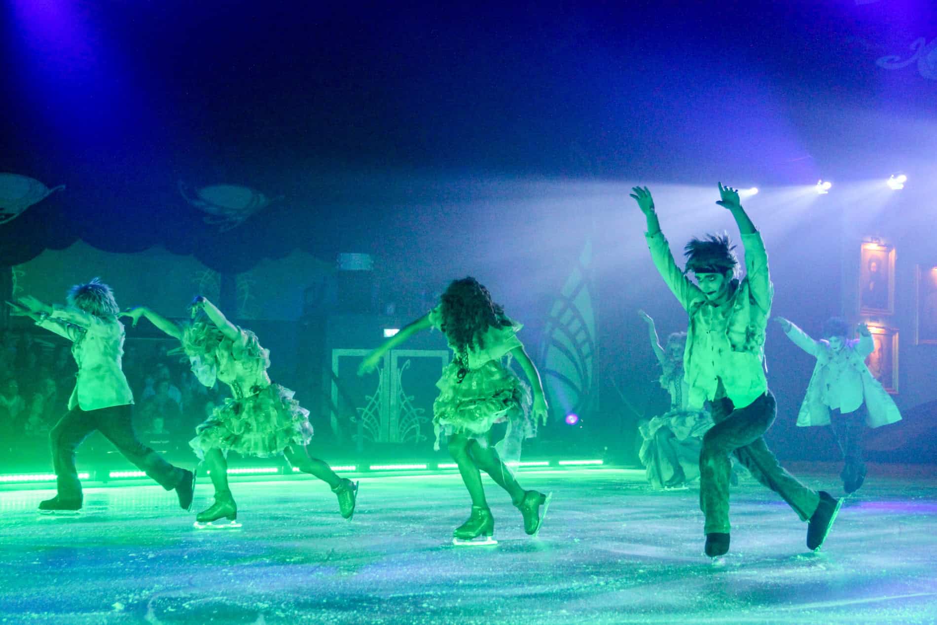 Ice skaters in mummy-like Halloween costume performing a show under blue-green lights. 