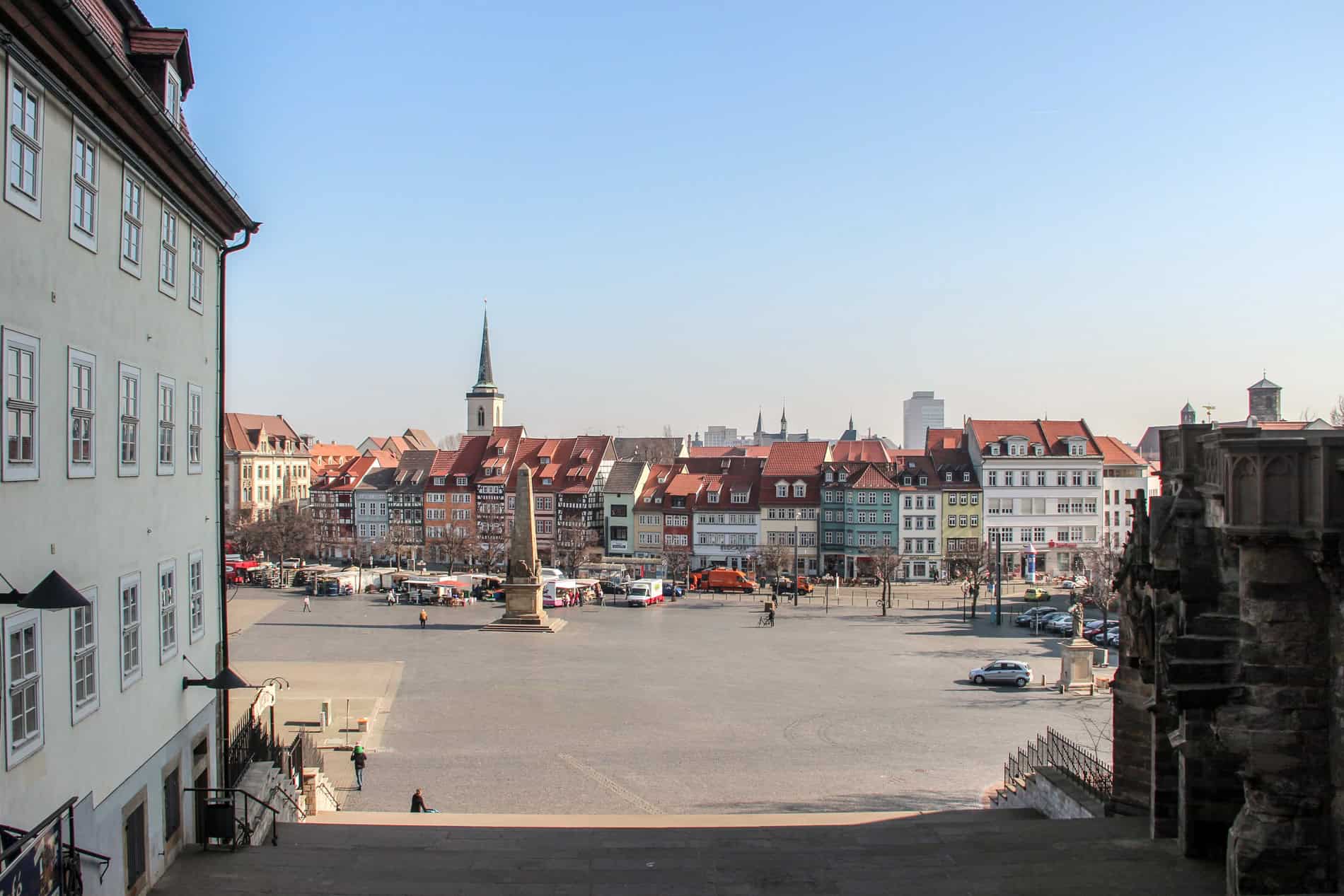 View from a staircase towards the Domplatz square in Erfurt, lined with colourful Renaissance houses and a church spire. 