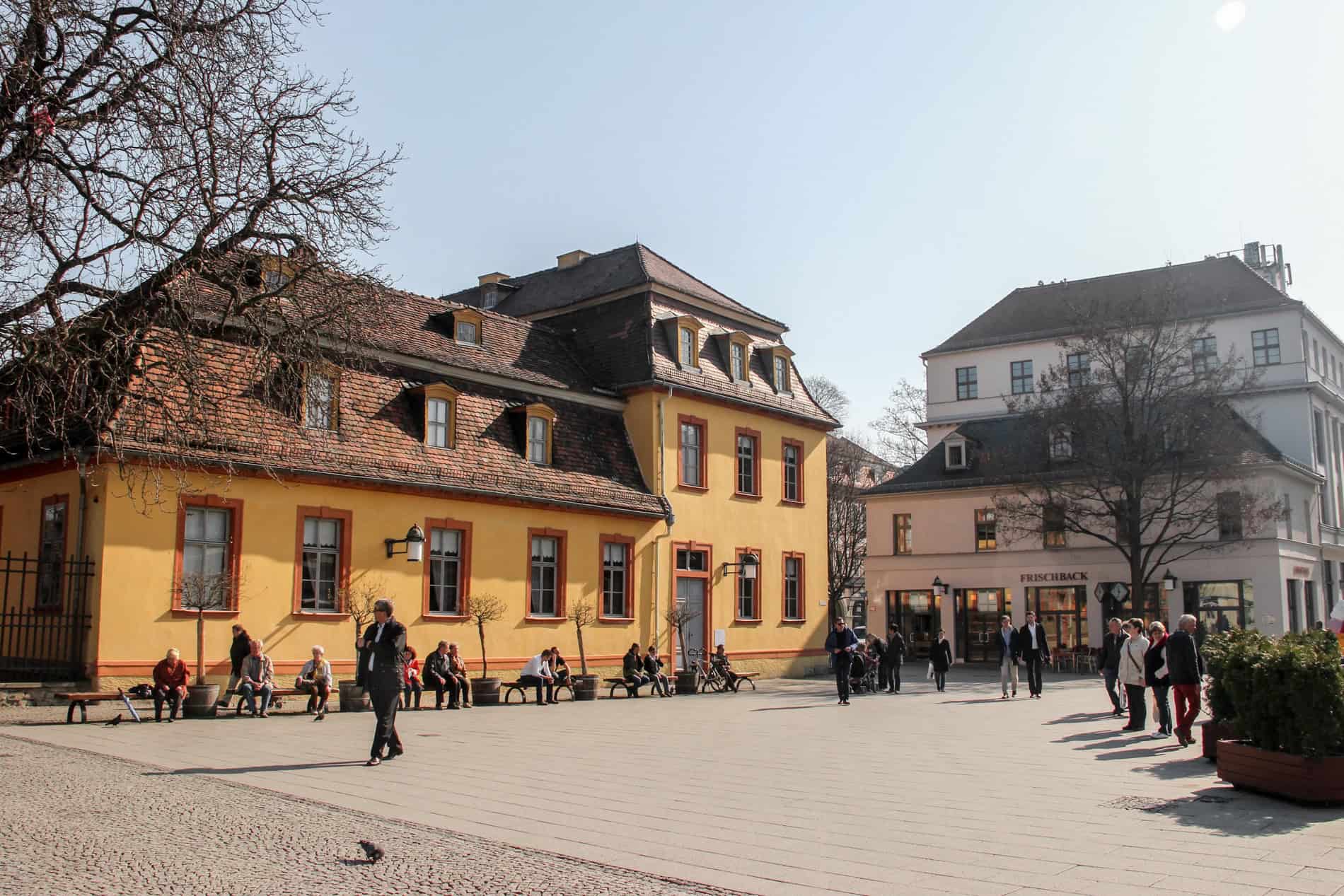 People outside a yellow painted, red brick roofed building in Weimar. 