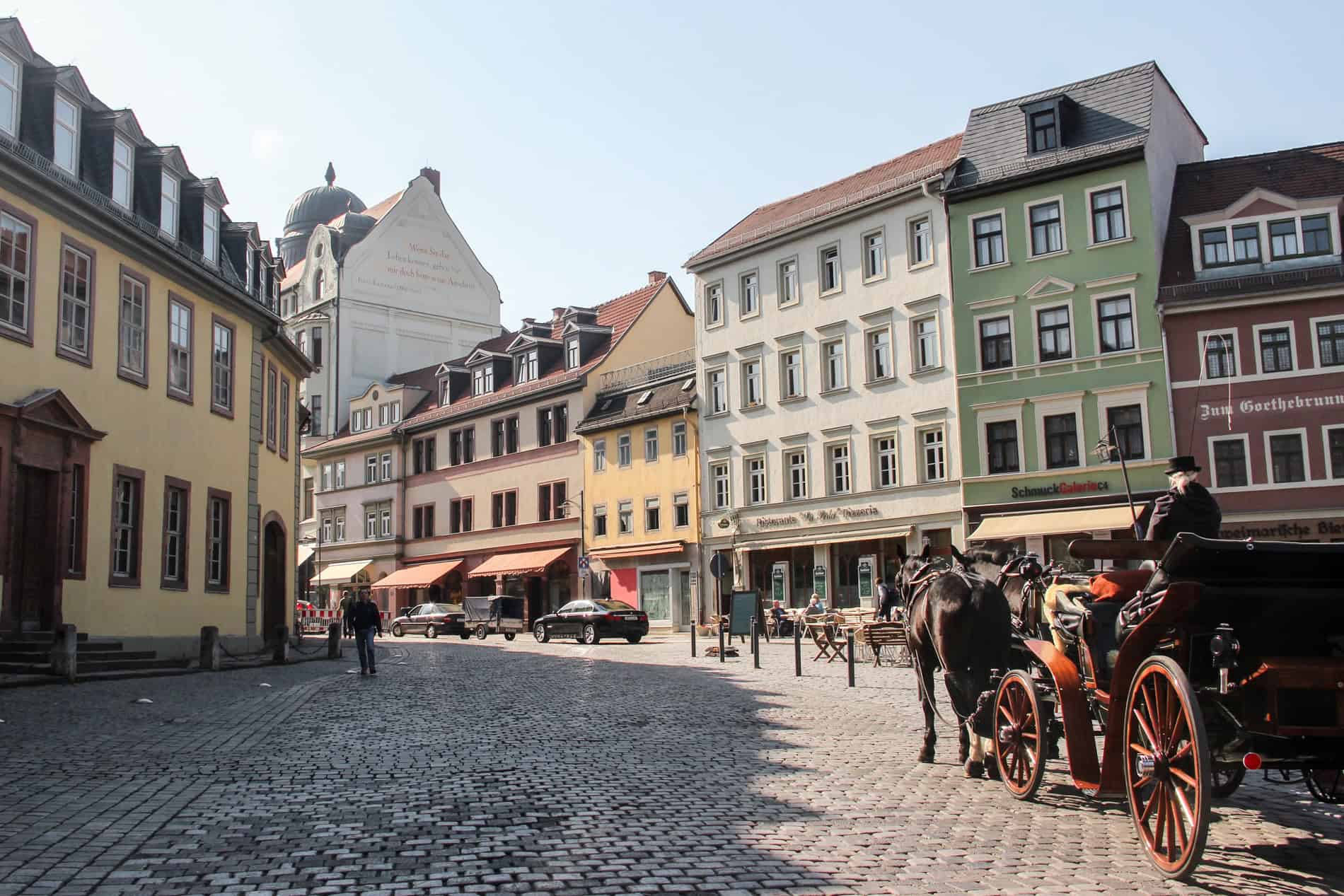 A horse and carriage rides on a cobblestoned street in front of earthy coloured buildings. 