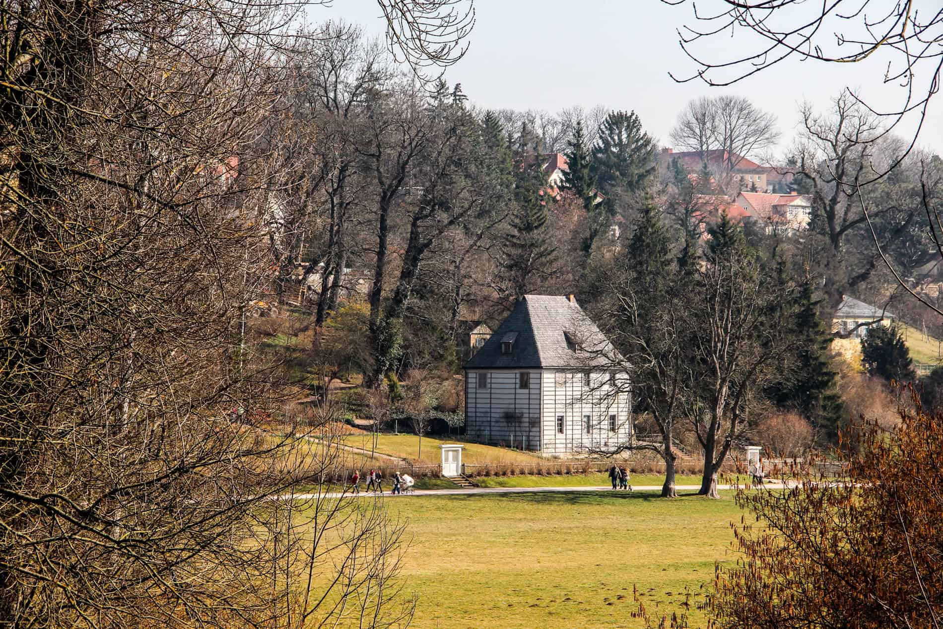A white house with a black roof standing alone in a big public garden. 