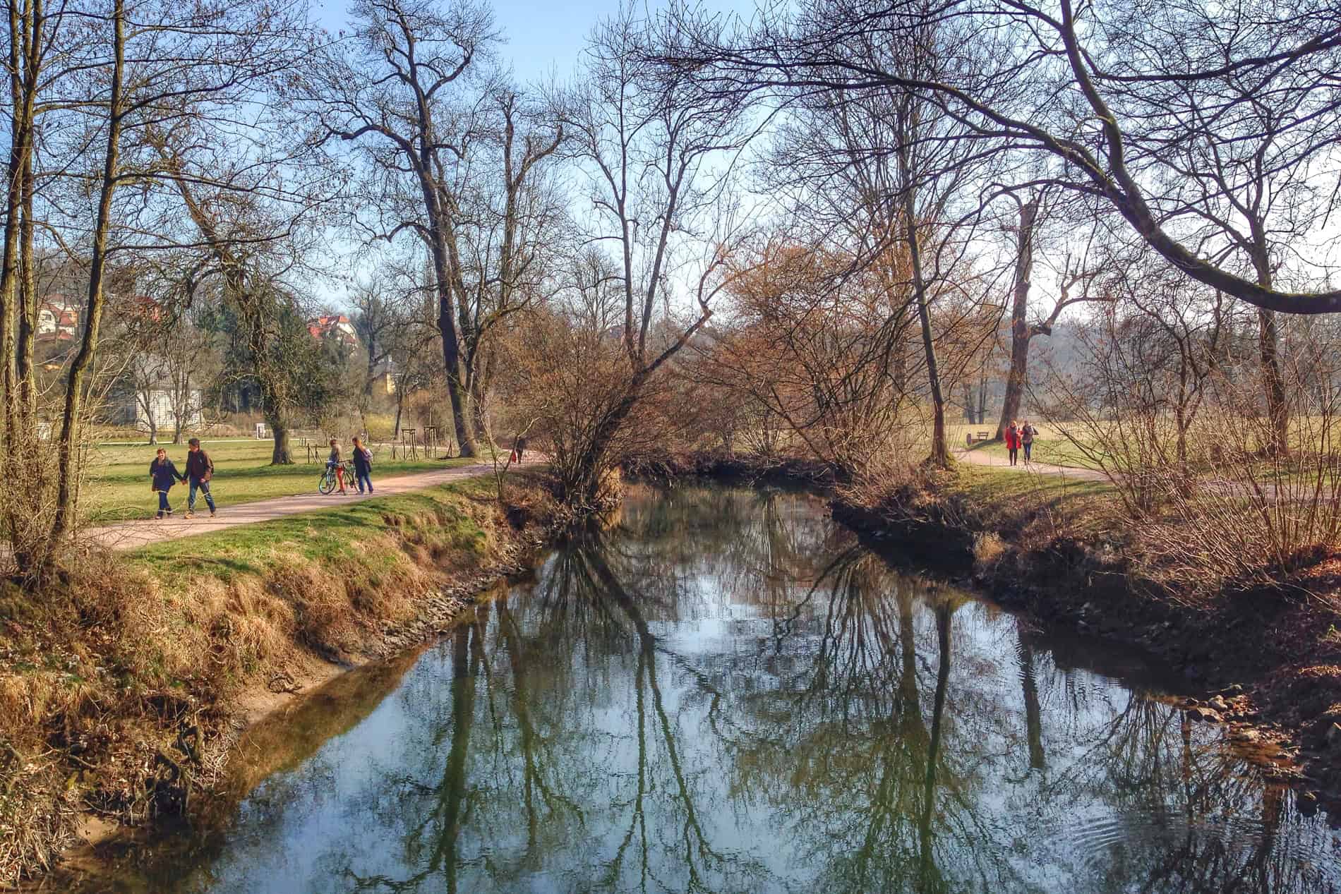 People walking on two pathways either side of a river in a large public path. 