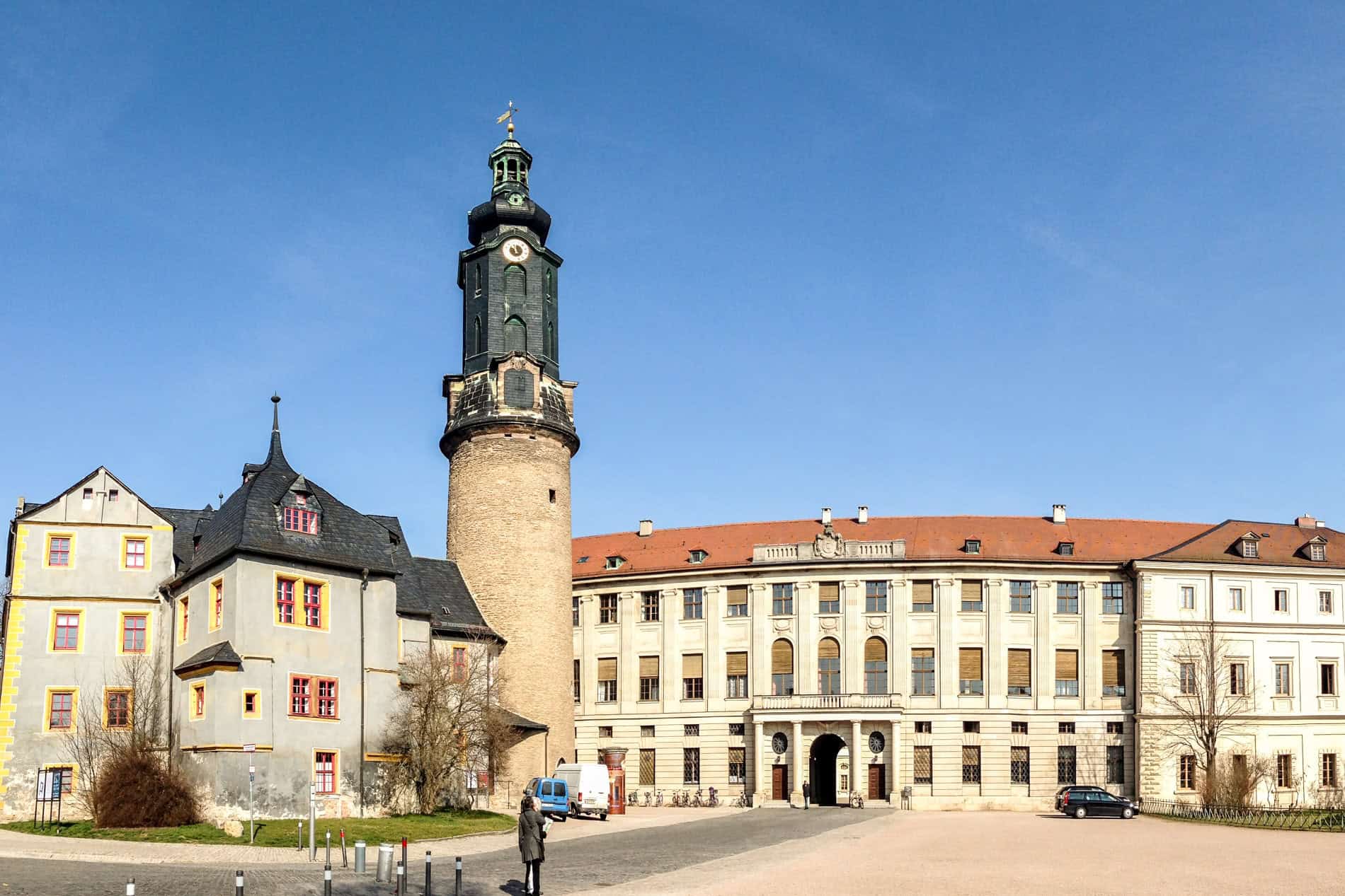 A baroque house, black spired tower and long green building of a German castle complex. 