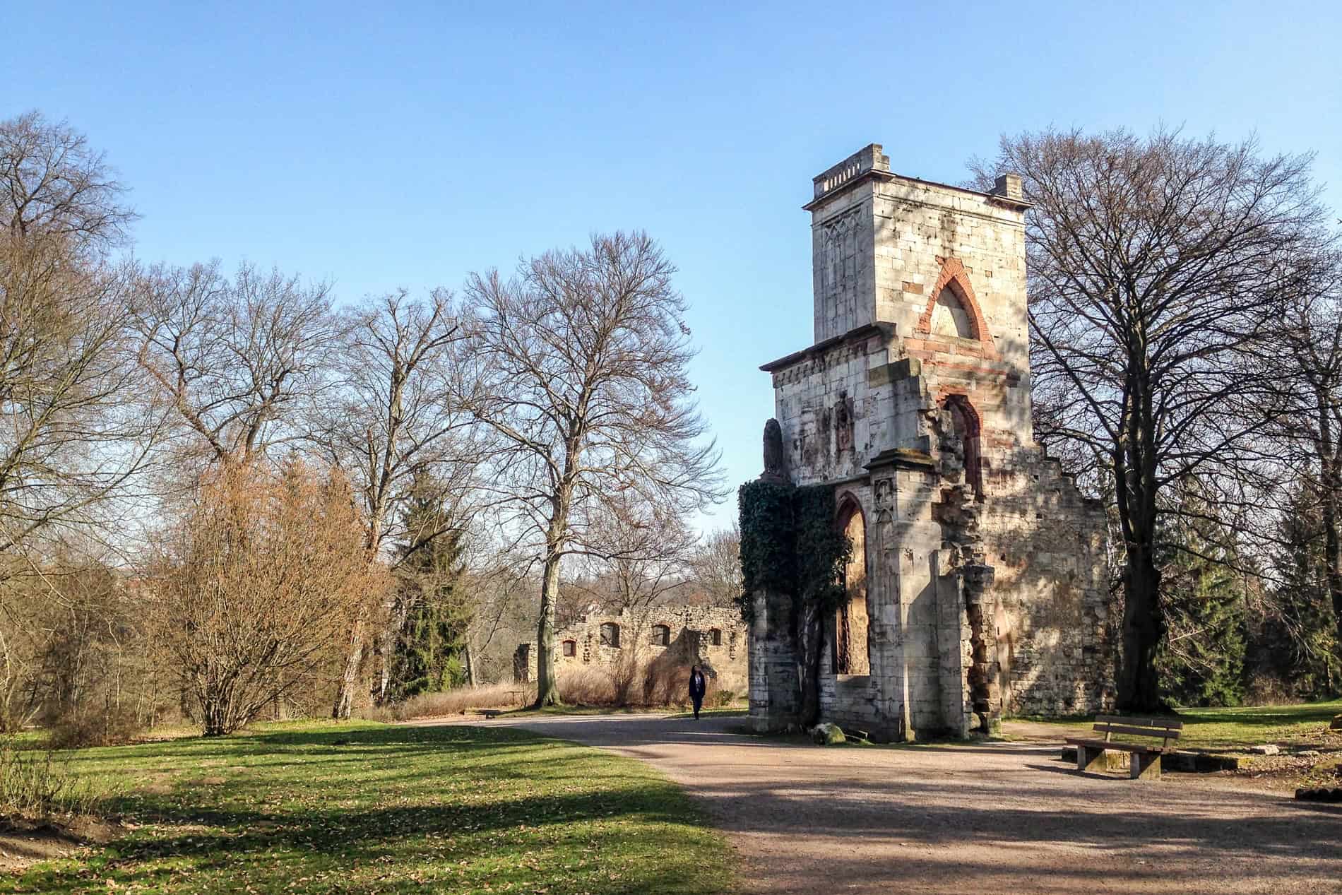 Ruins of a tall building turret in a large green path with sparse trees. 