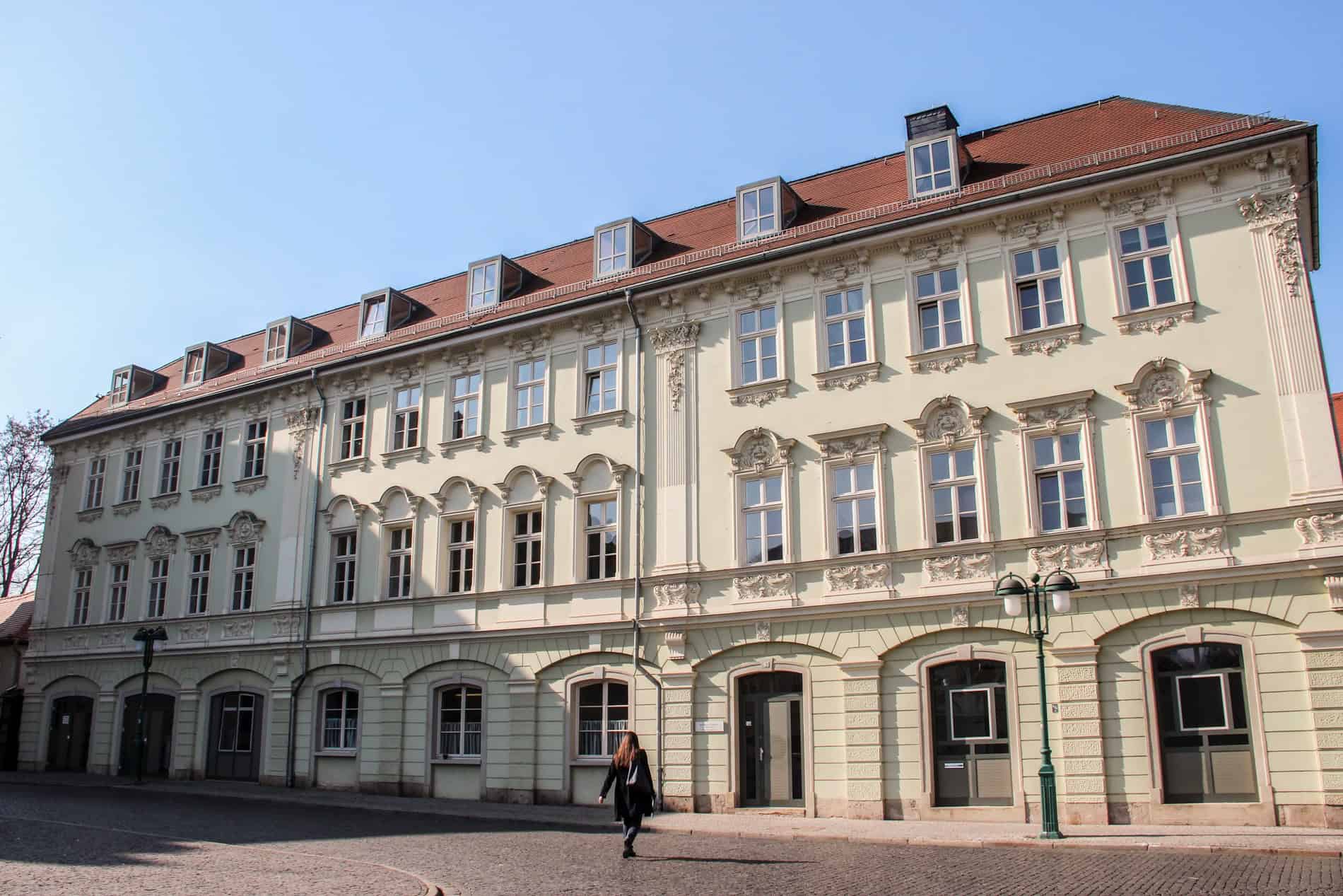 A woman walking towards the entrance of the light green decorated facade of the University of Music Franz Liszt, inWeimar.