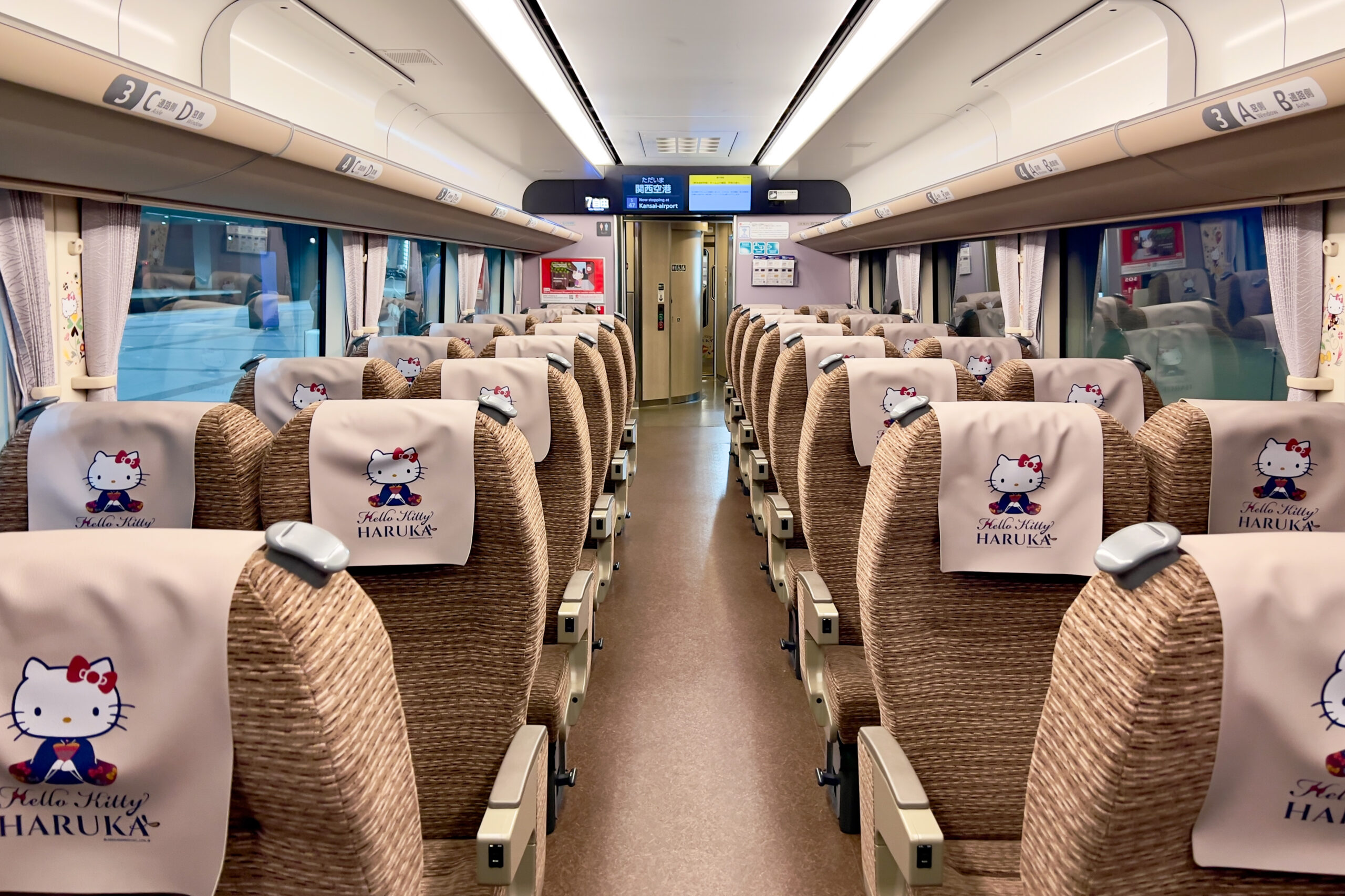 Interior of the Hello Kitty HARUKA train showing mocha-coloured fabric seats with Hello Kitty-branded headrests and themed wall decorations