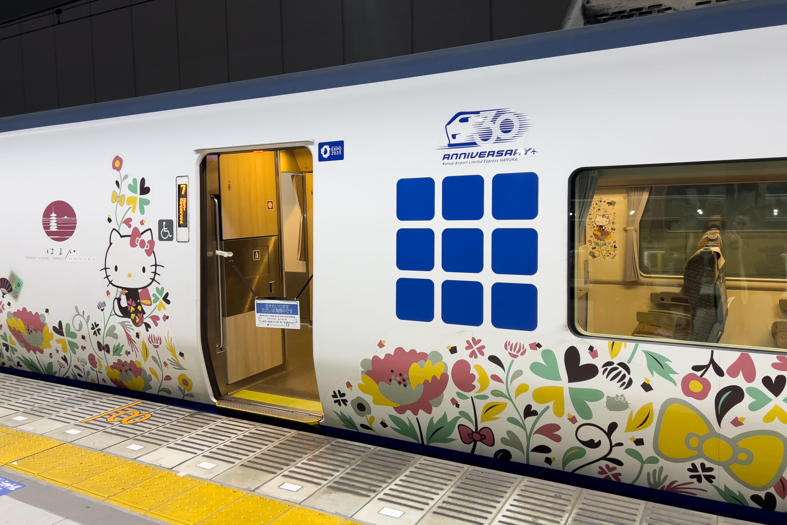 Hello Kitty HARUKA limited express train at a station platform, with a white and pastel-coloured exterior covered in cheerful Hello Kitty and floral motifs.