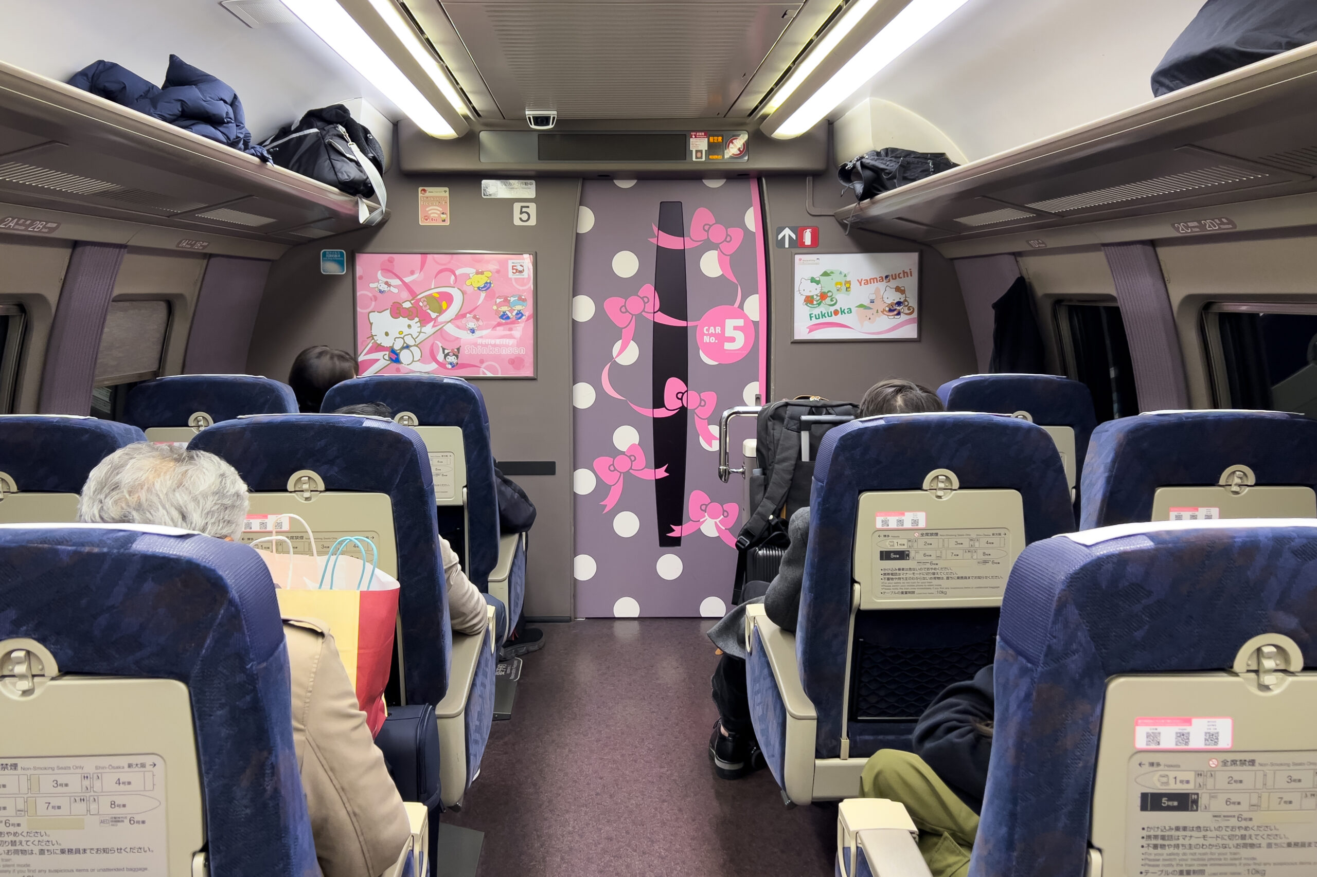Interior view of the Hello Kitty Shinkansen reserved seating carriage featuring blue seating and Hello Kitty themed wall and door graphics.