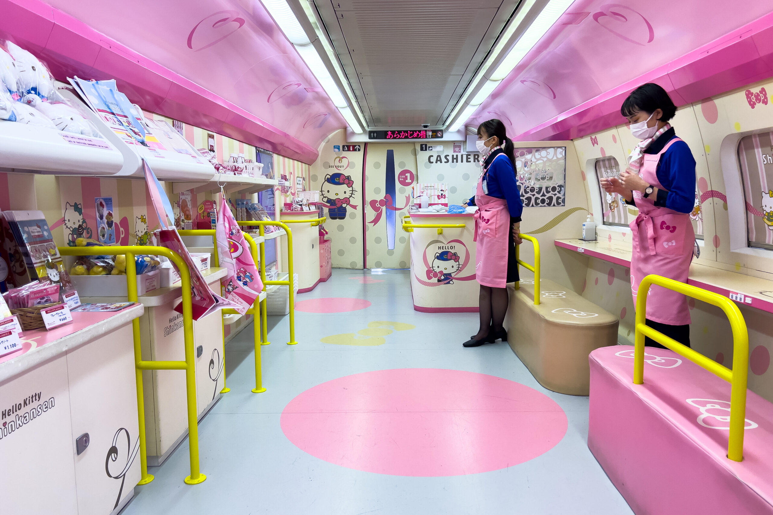 Inside the Hello! Plaza carriage of the Hello Kitty Shinkansen train showcasing a small pastel and bold pink shop area with Hello Kitty merchandise, decorations, and themed displays.