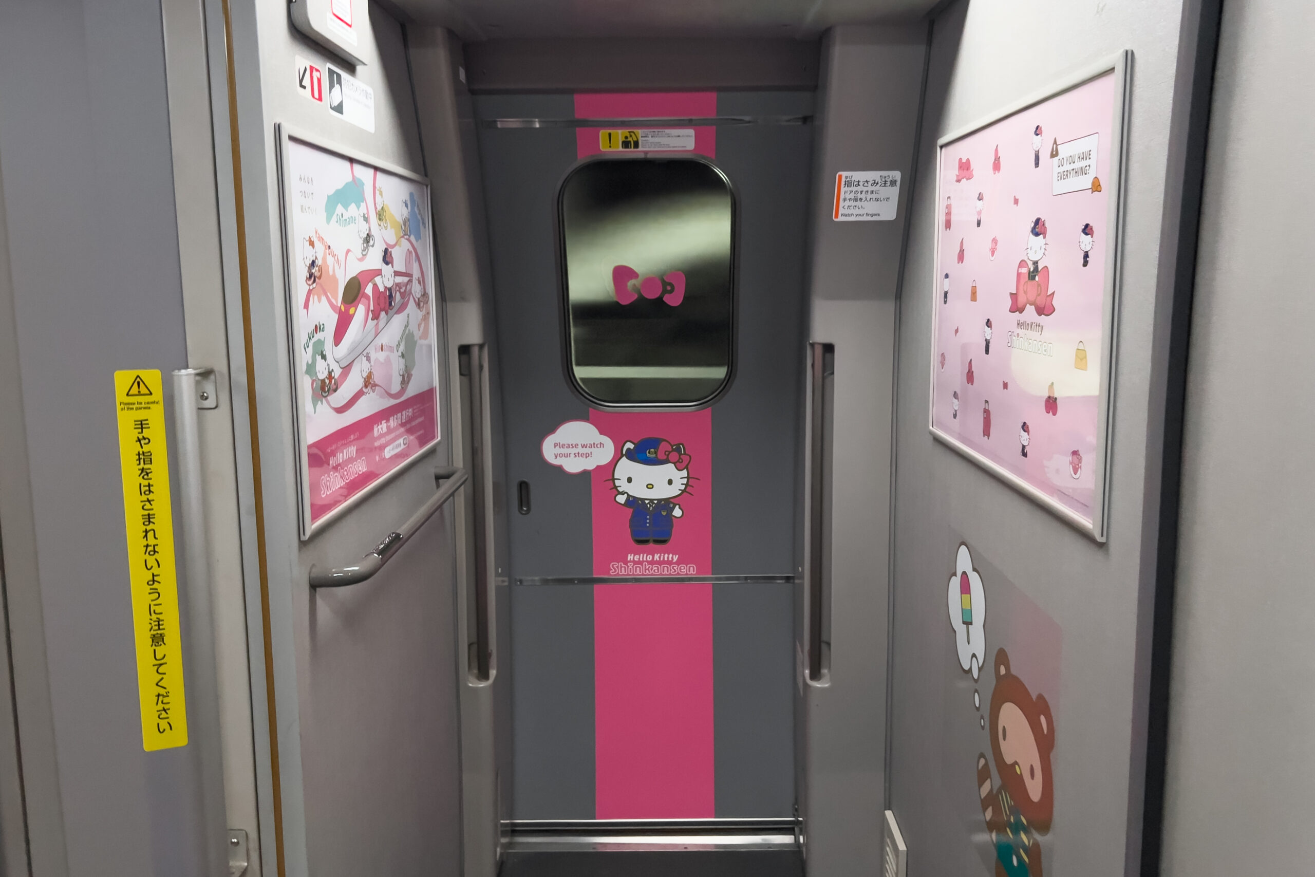 Interior view of the train doors of the Hello Kitty Shinkansen with a pink stripe Hello Kitty graphics and wall posters.