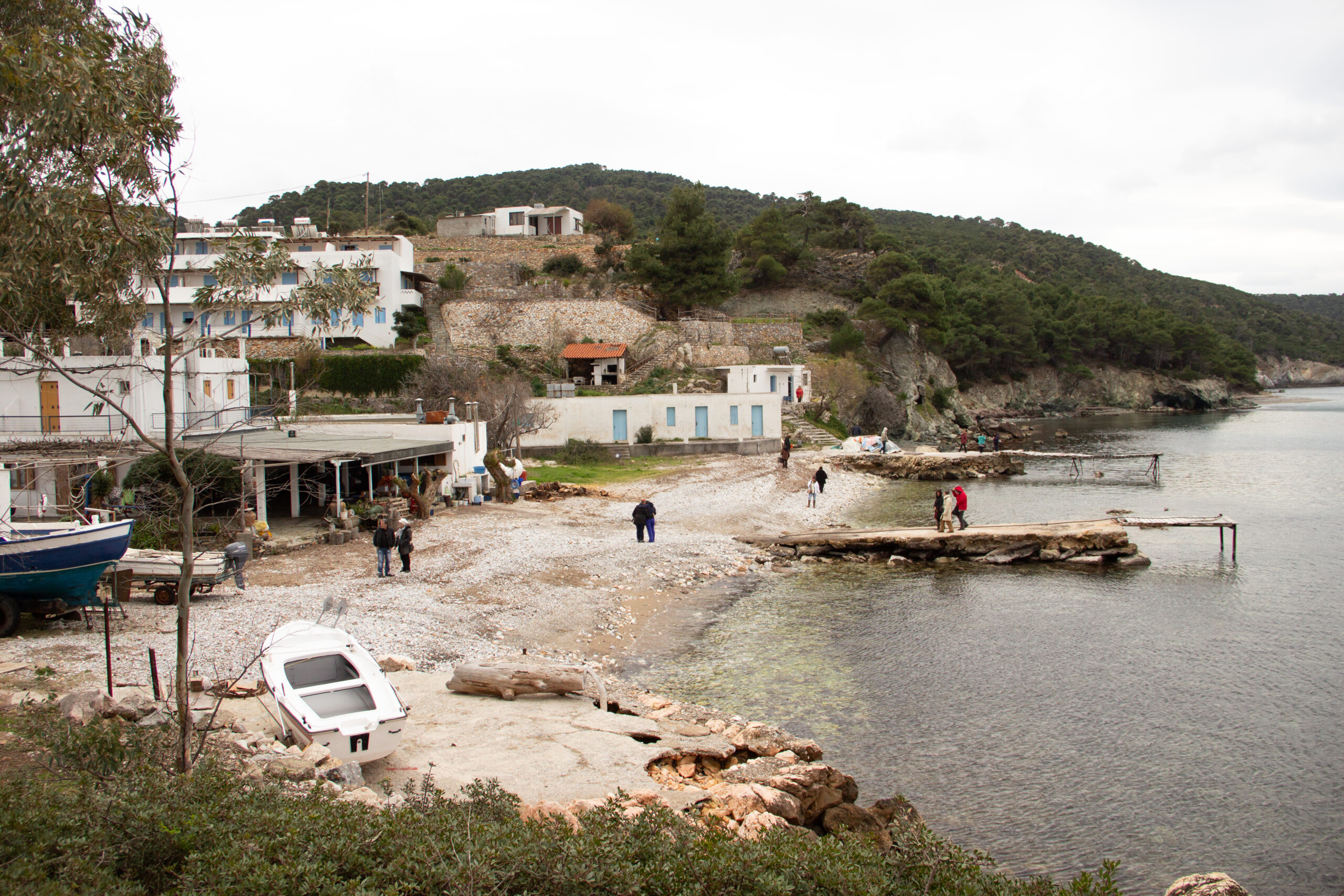 People walking in a tiny, rock-strewn bay with small jetties and empty boats.