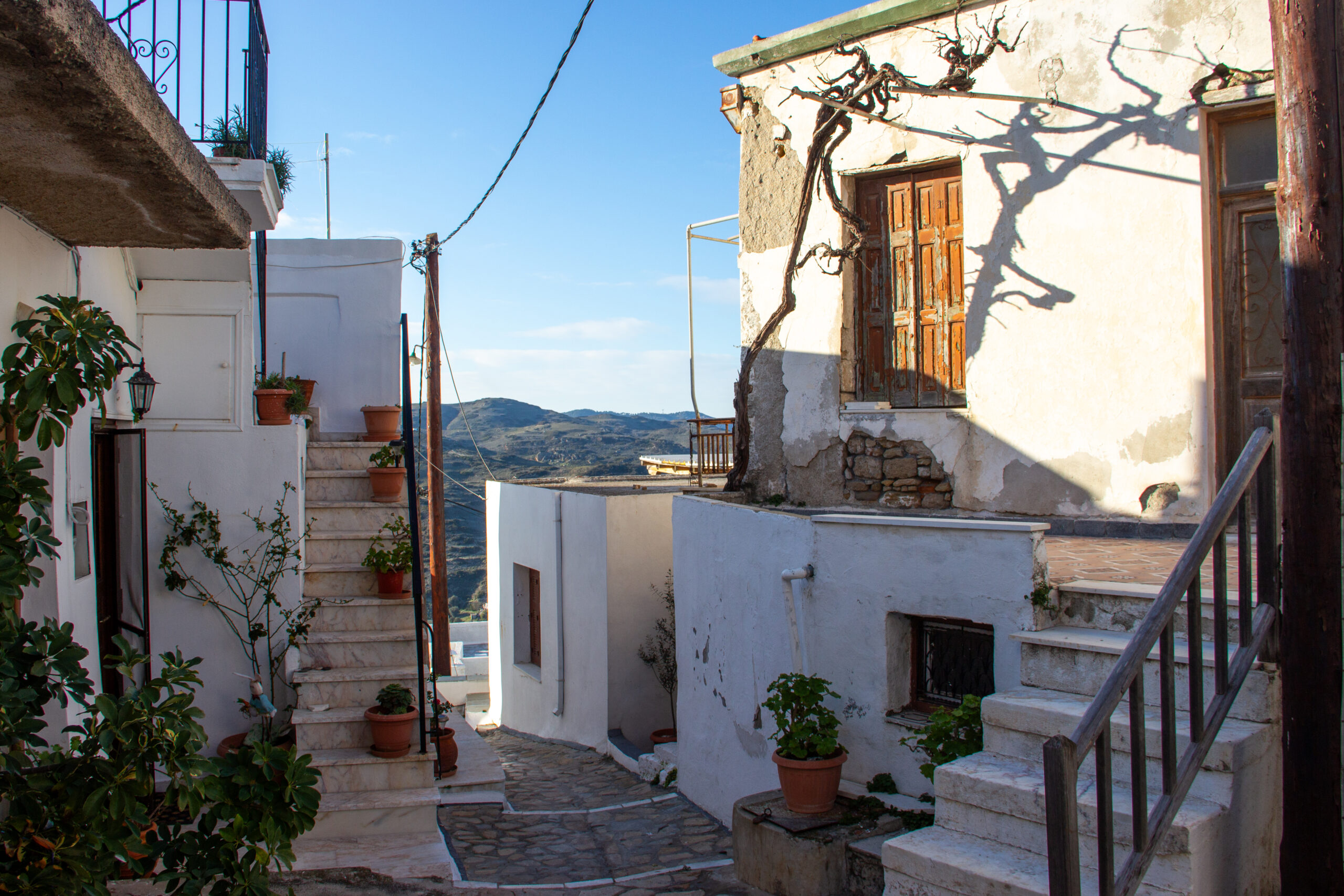 A picturesque street scene of Skyros Chora village with white houses decorated with wooden window and door elements and scattered with plant pots.