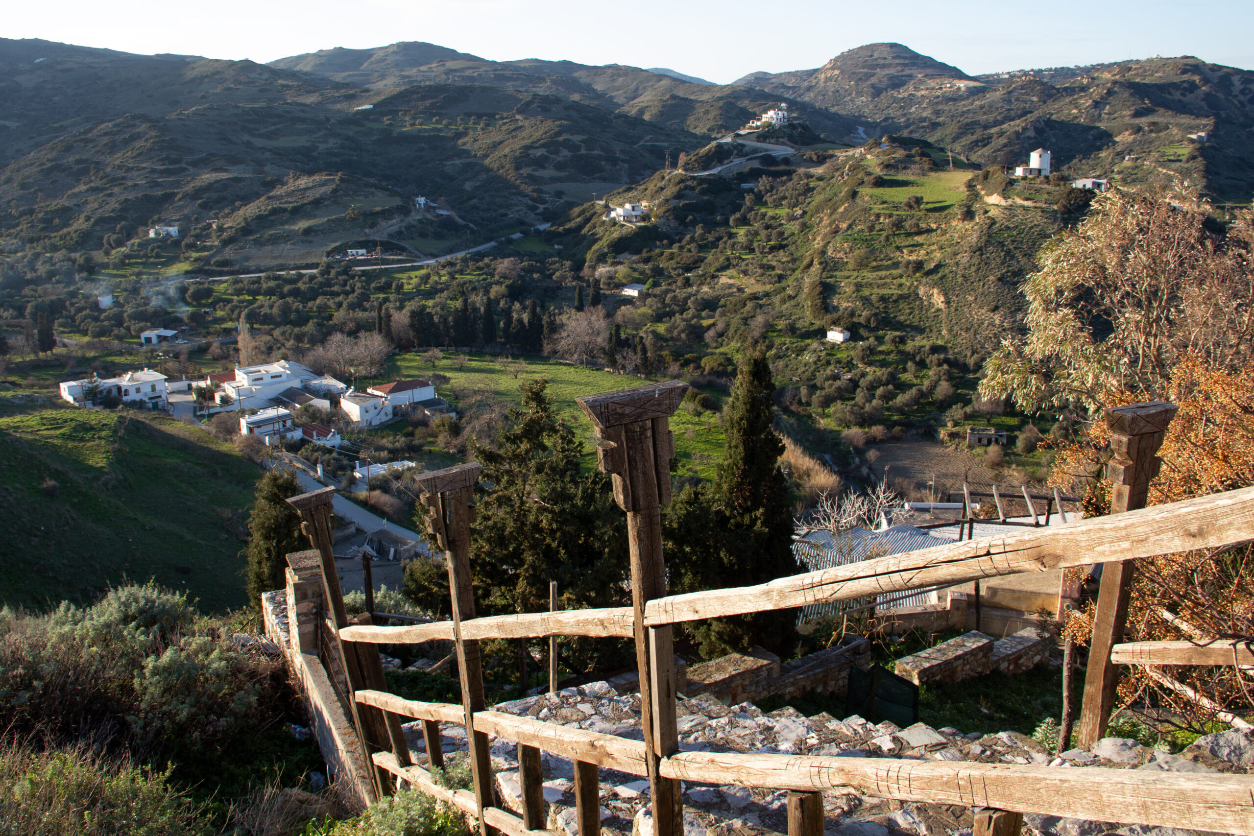 Elevated view from a stone-step pathway looking over the rolling green on Skyros Island and a small cluster of white houses.