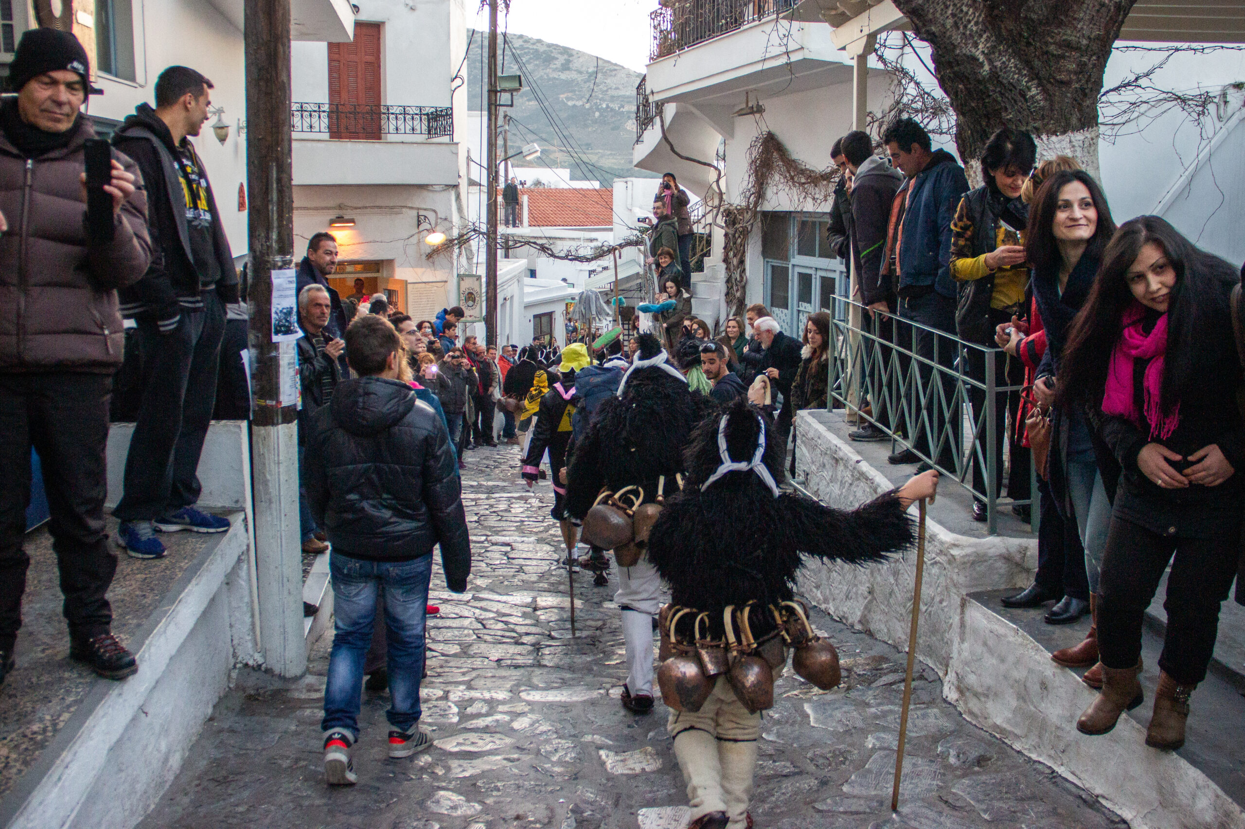 Goatman costumed performers descending a cobbled street in Skyros town as spectators look on.