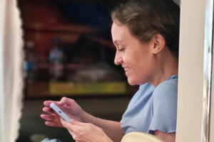 Smiling woman using a smartphone while sitting in a modern sleeper bus cabin with privacy curtains.